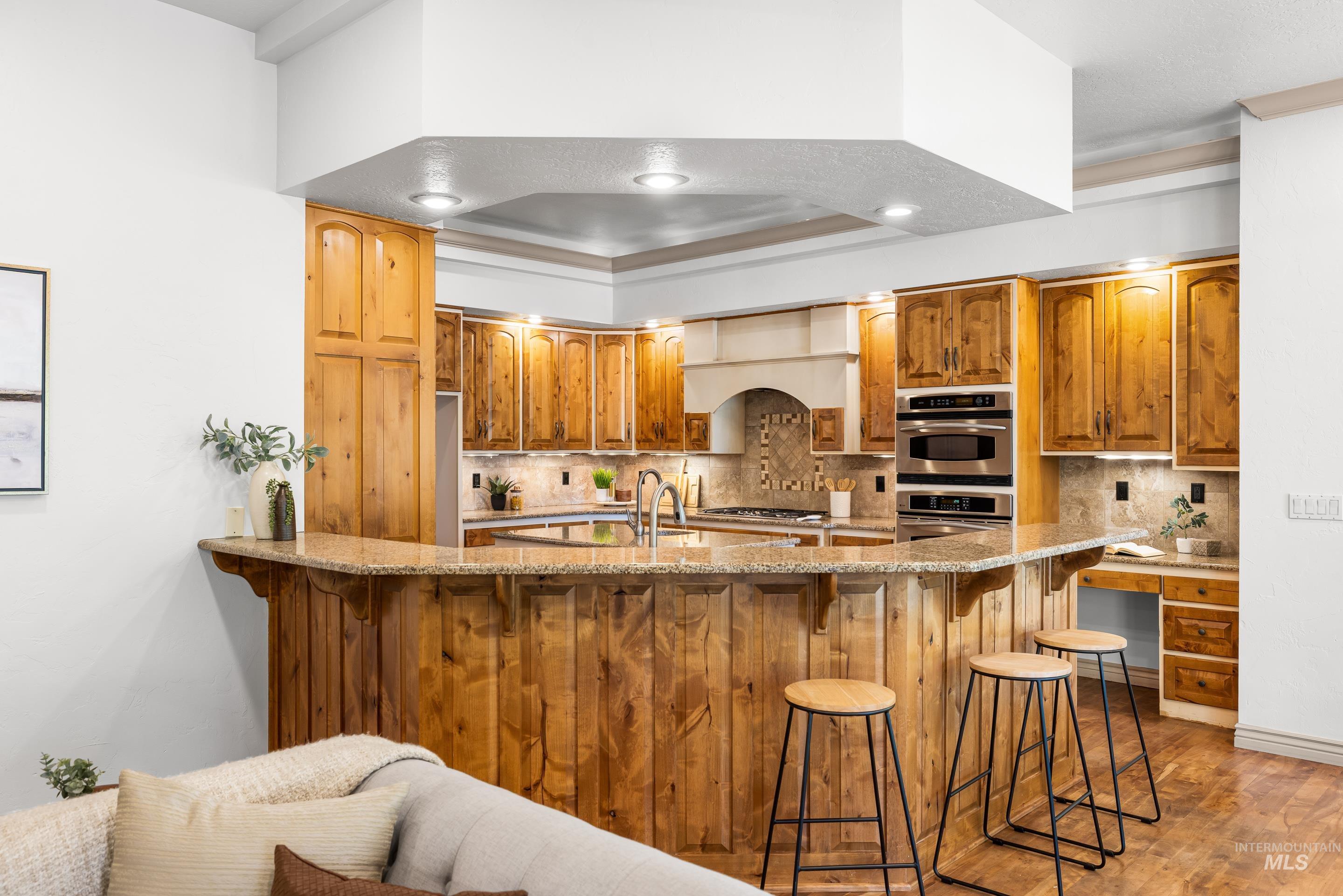 Kitchen with backsplash, a breakfast bar area, light stone counters, brown cabinets, and light wood finished floors