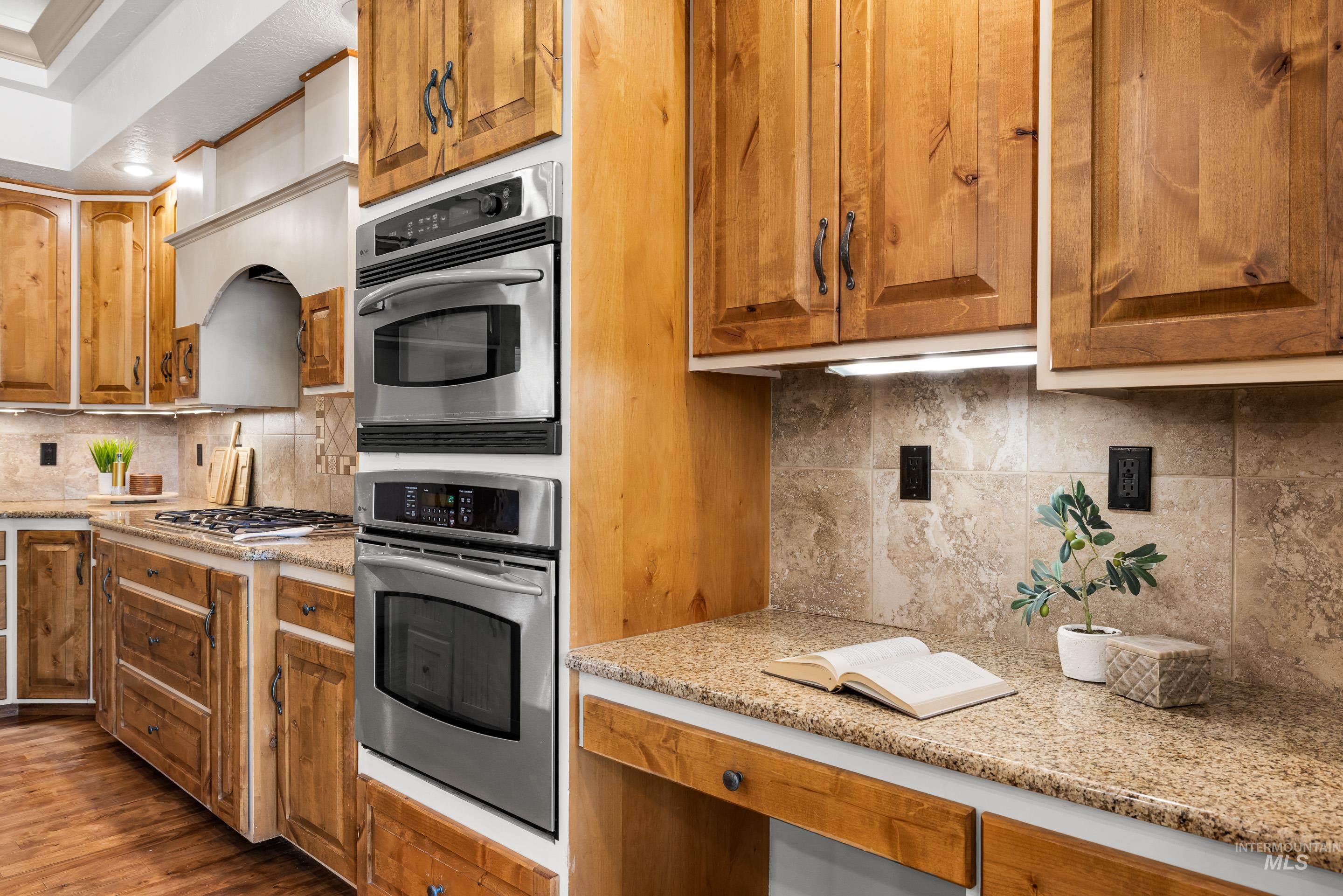 Kitchen with decorative backsplash, light stone counters, and brown cabinets
