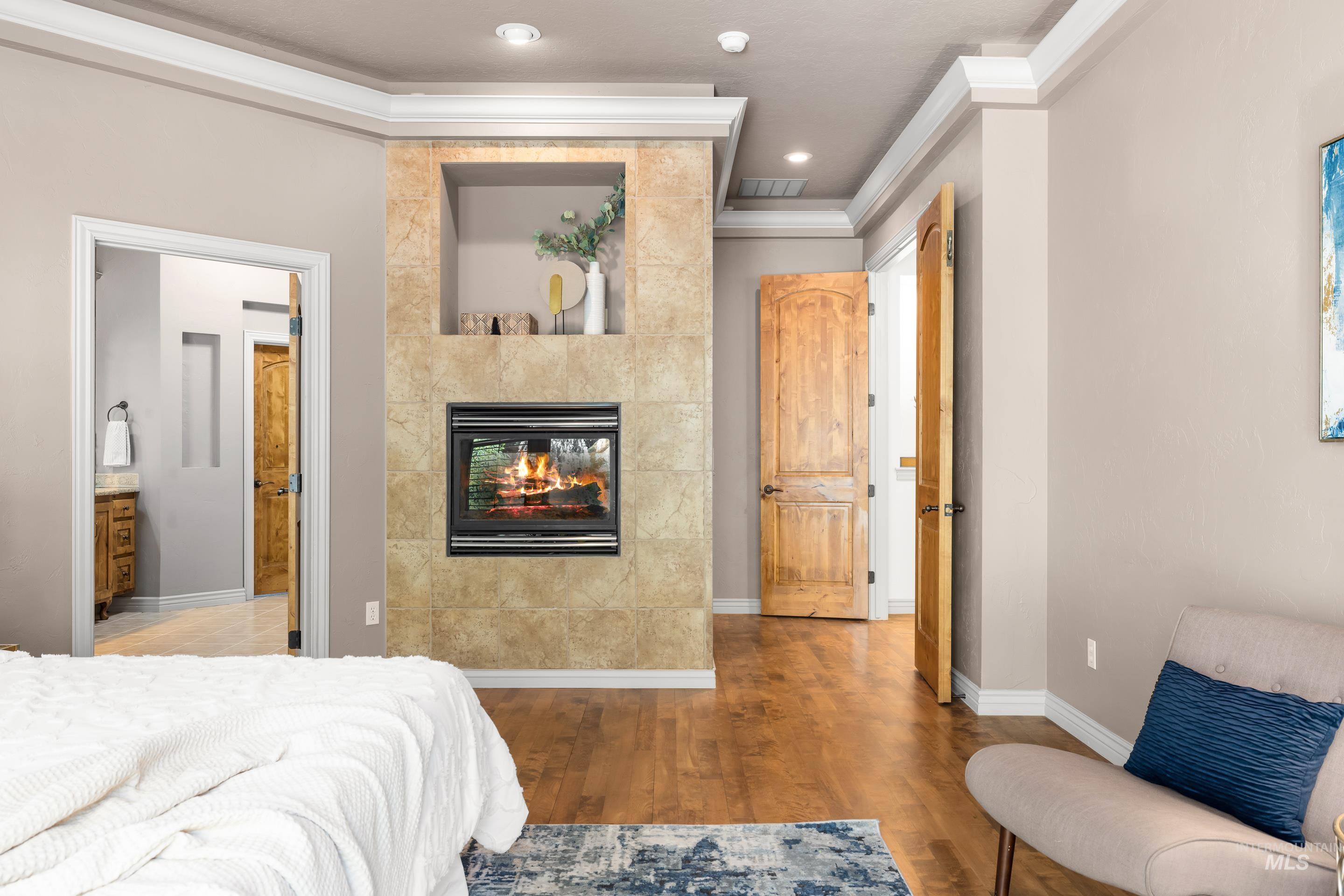 Bedroom with wood finished floors, crown molding, a tile fireplace, ensuite bath, and recessed lighting