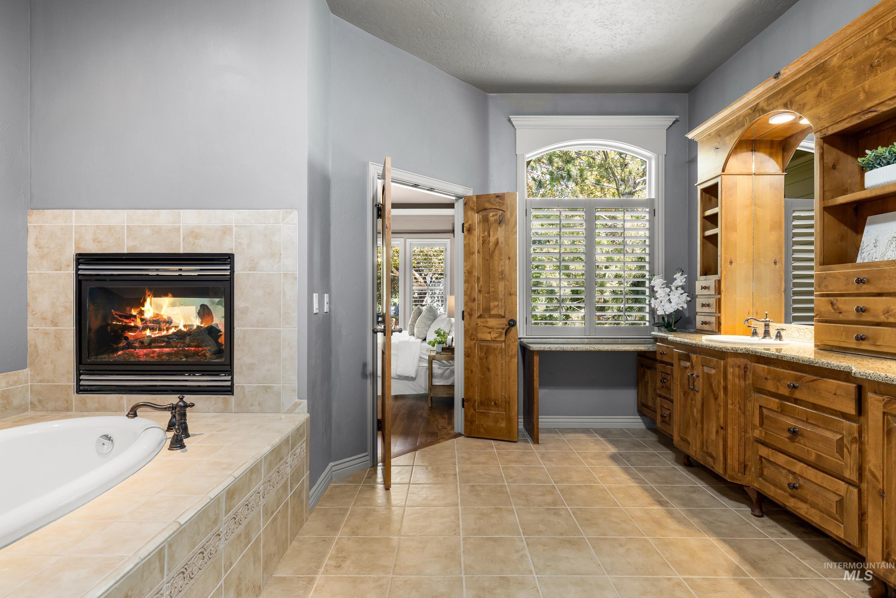 Full bathroom featuring light tile patterned flooring, vanity, a fireplace, a bath, and connected bathroom