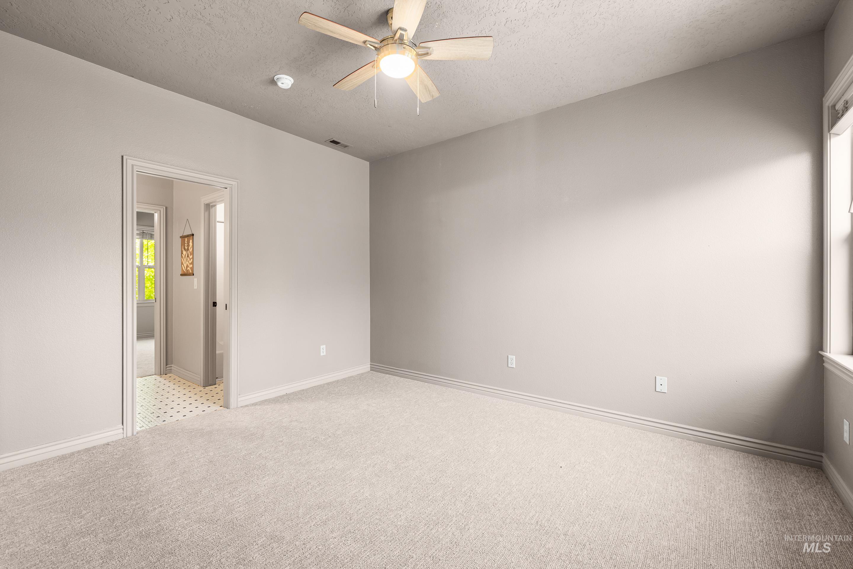 Unfurnished bedroom featuring a textured ceiling, light colored carpet, and ceiling fan