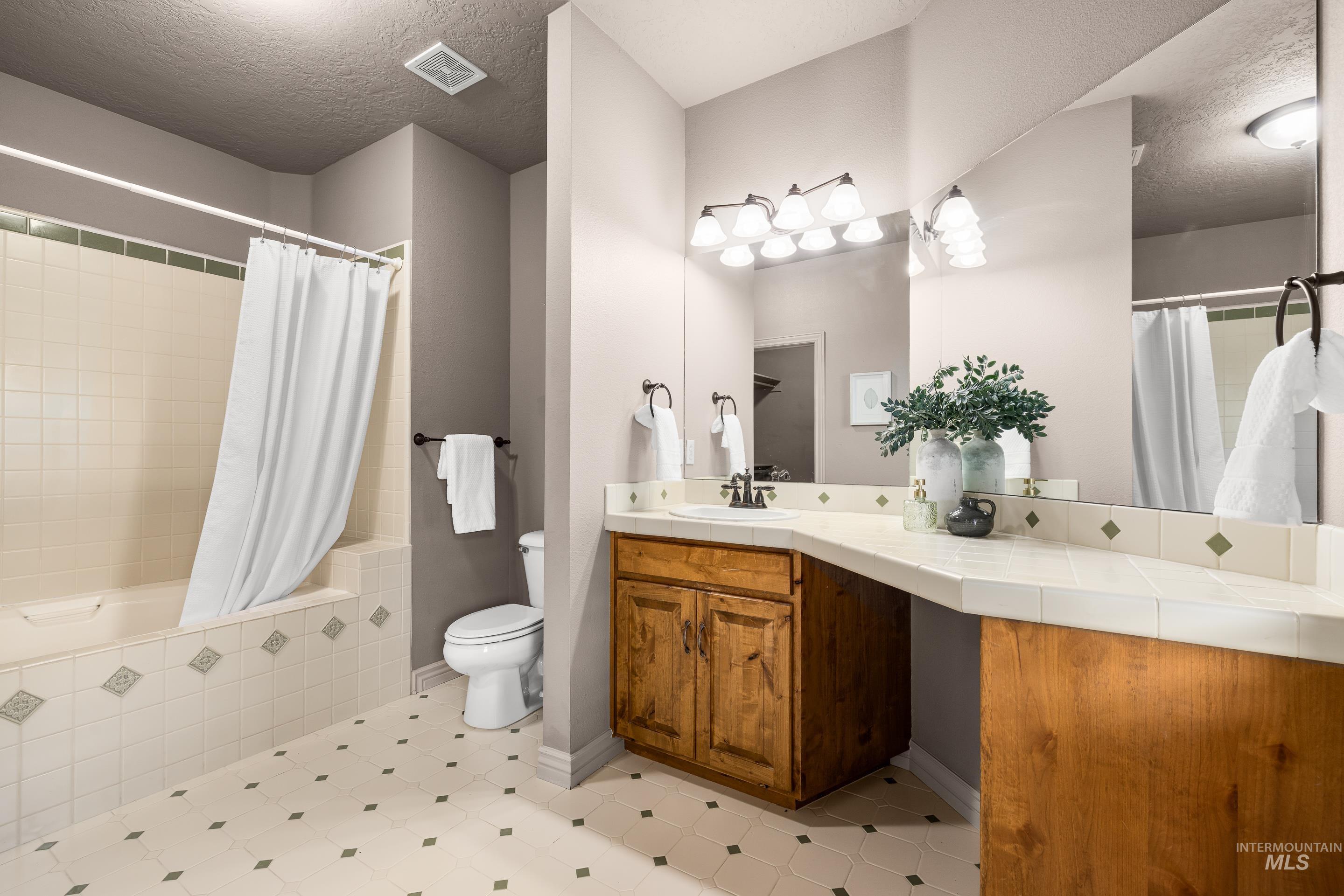 Bathroom with a textured ceiling, tiled shower / bath, and vanity