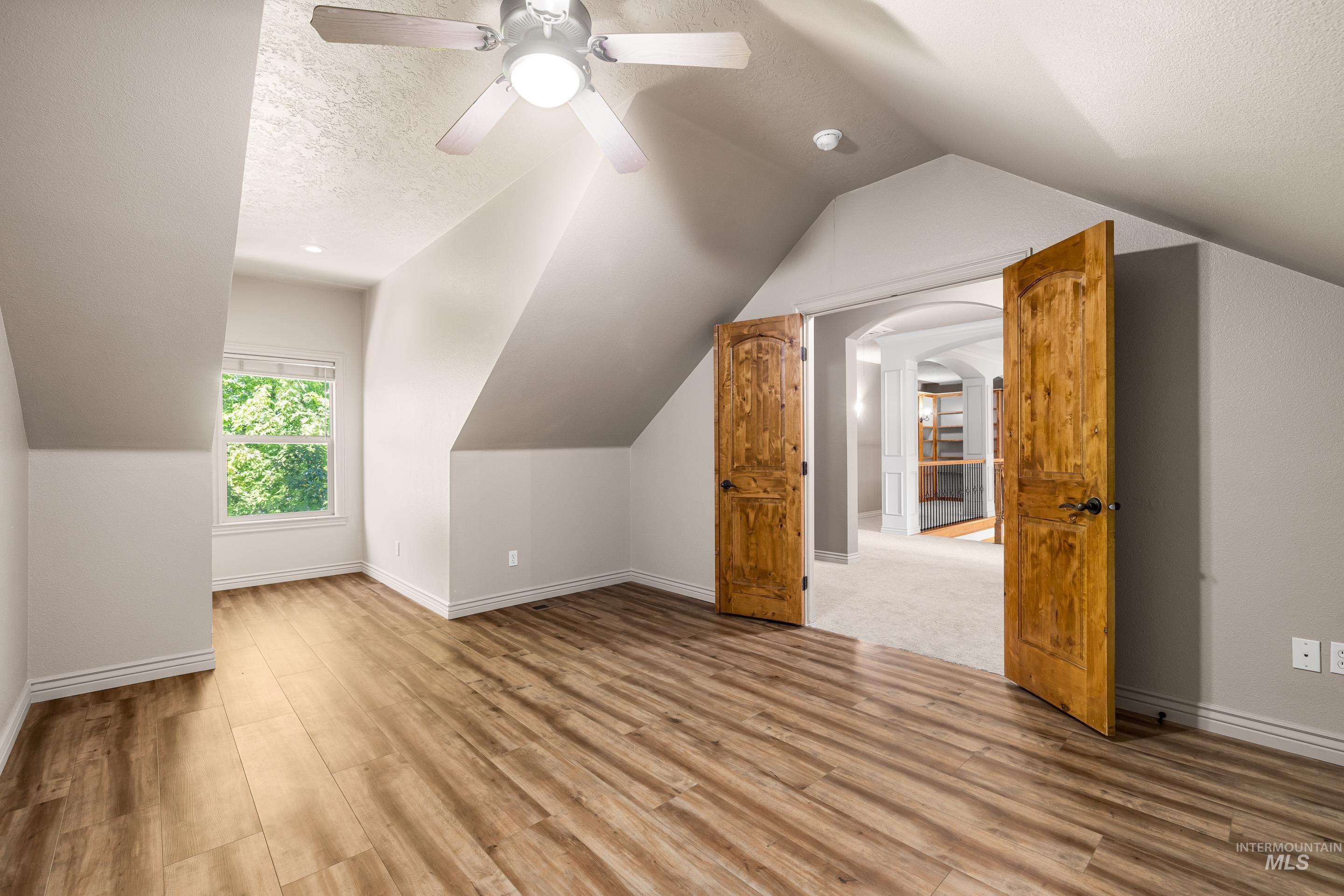 Additional living space featuring a textured ceiling, light wood-type flooring, vaulted ceiling, a ceiling fan, and arched walkways