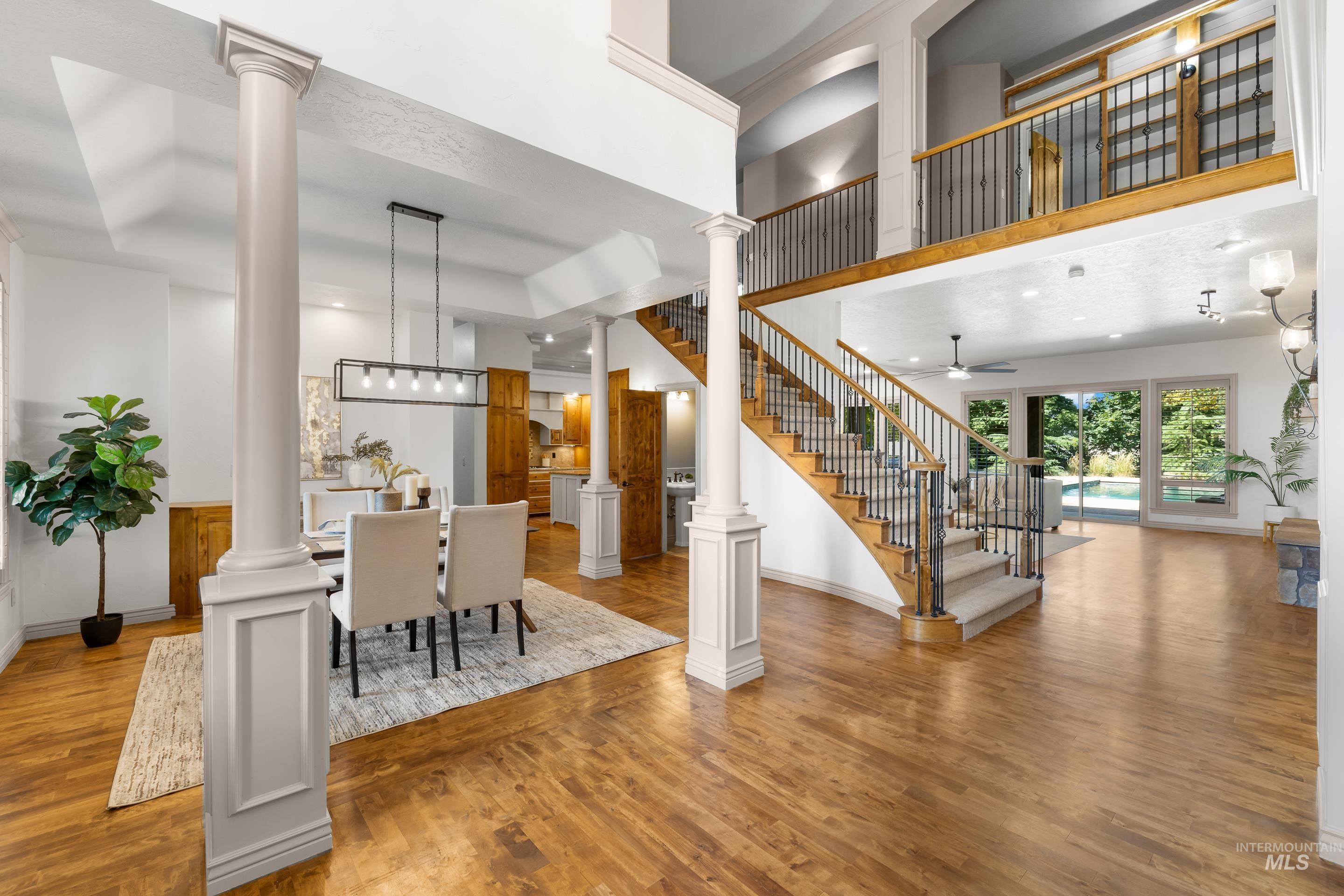 Dining room featuring ornate columns, light wood-style floors, stairway, ceiling fan, and a high ceiling