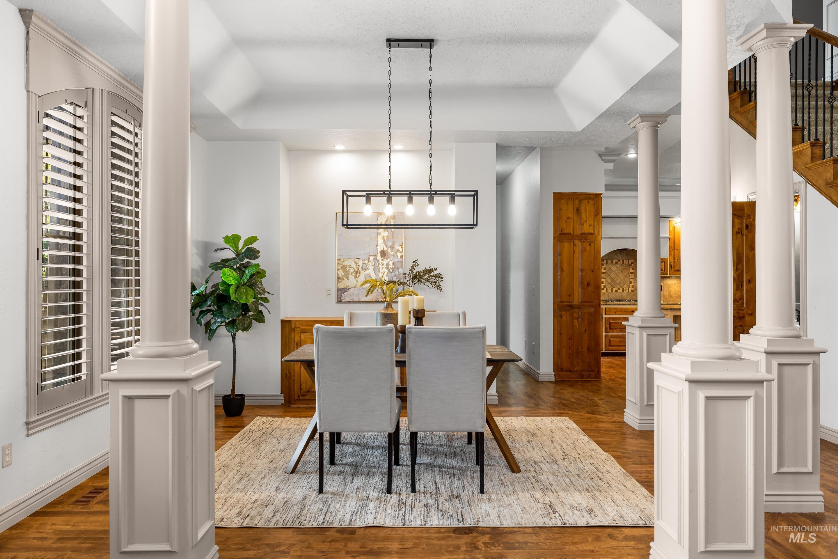 Dining space featuring ornate columns, a tray ceiling, and dark wood-style flooring