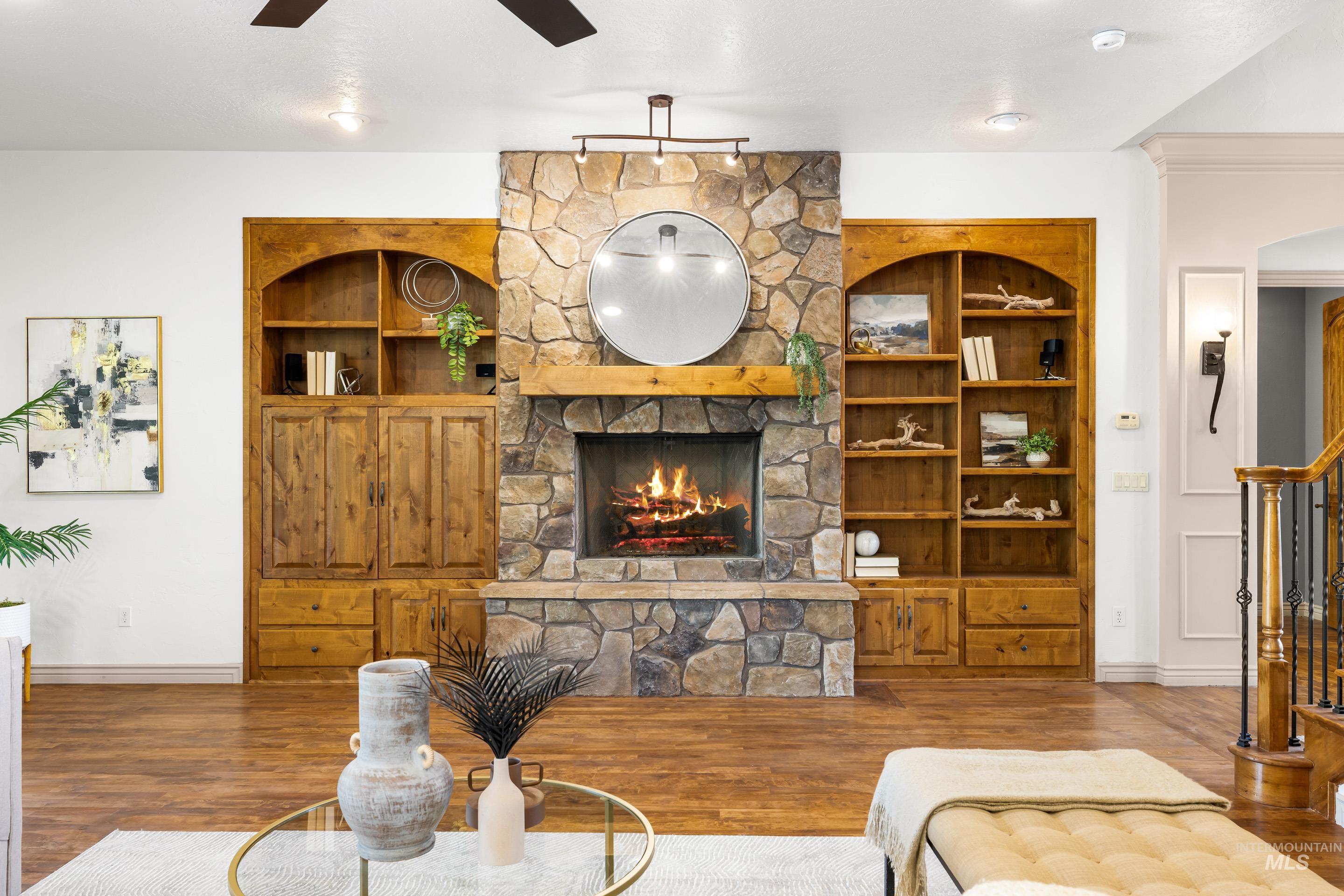 Living area with built in features, a stone fireplace, stairway, wood finished floors, and ceiling fan