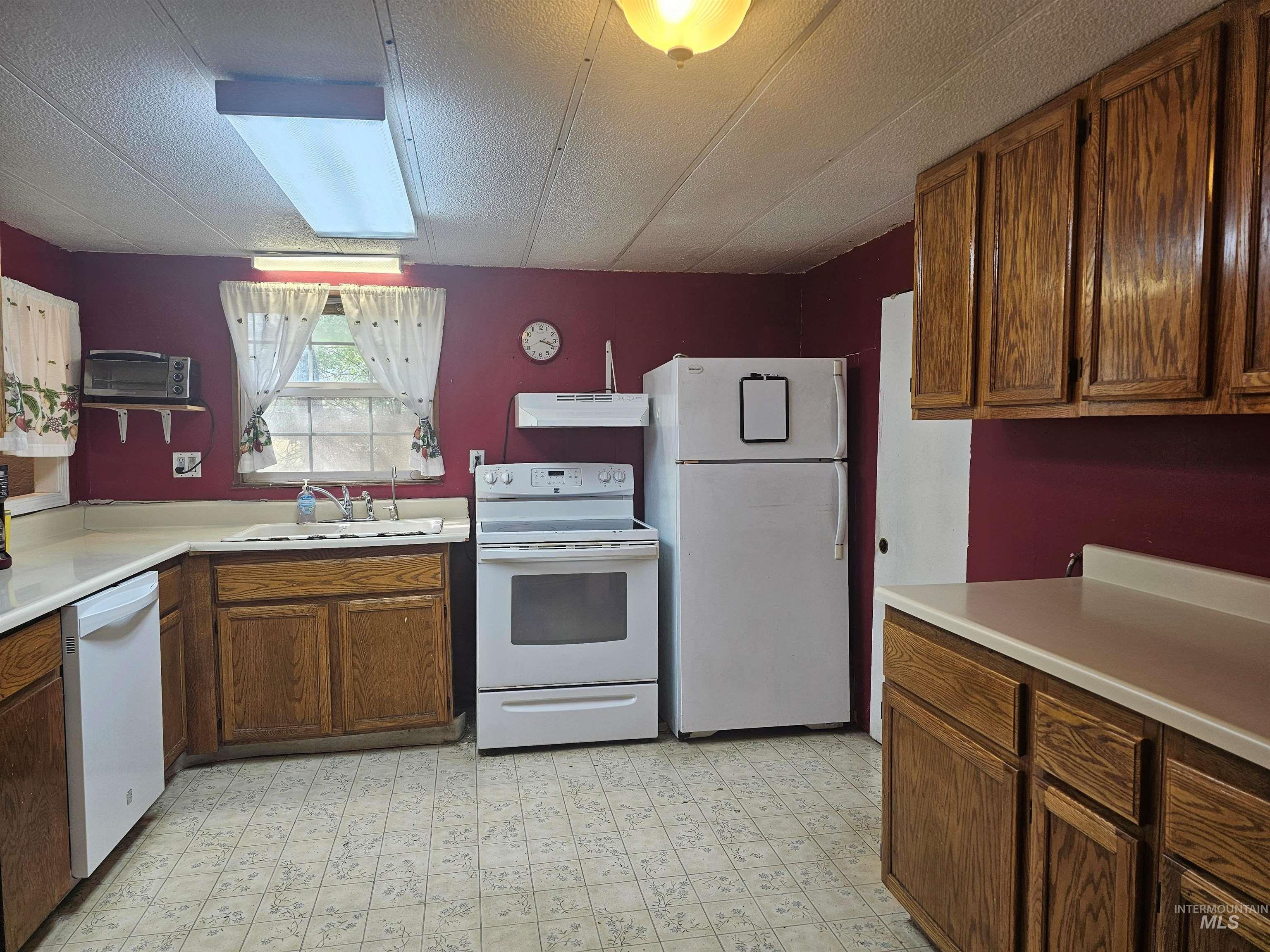 Kitchen featuring white appliances, light flooring, light countertops, a textured ceiling, and brown cabinets