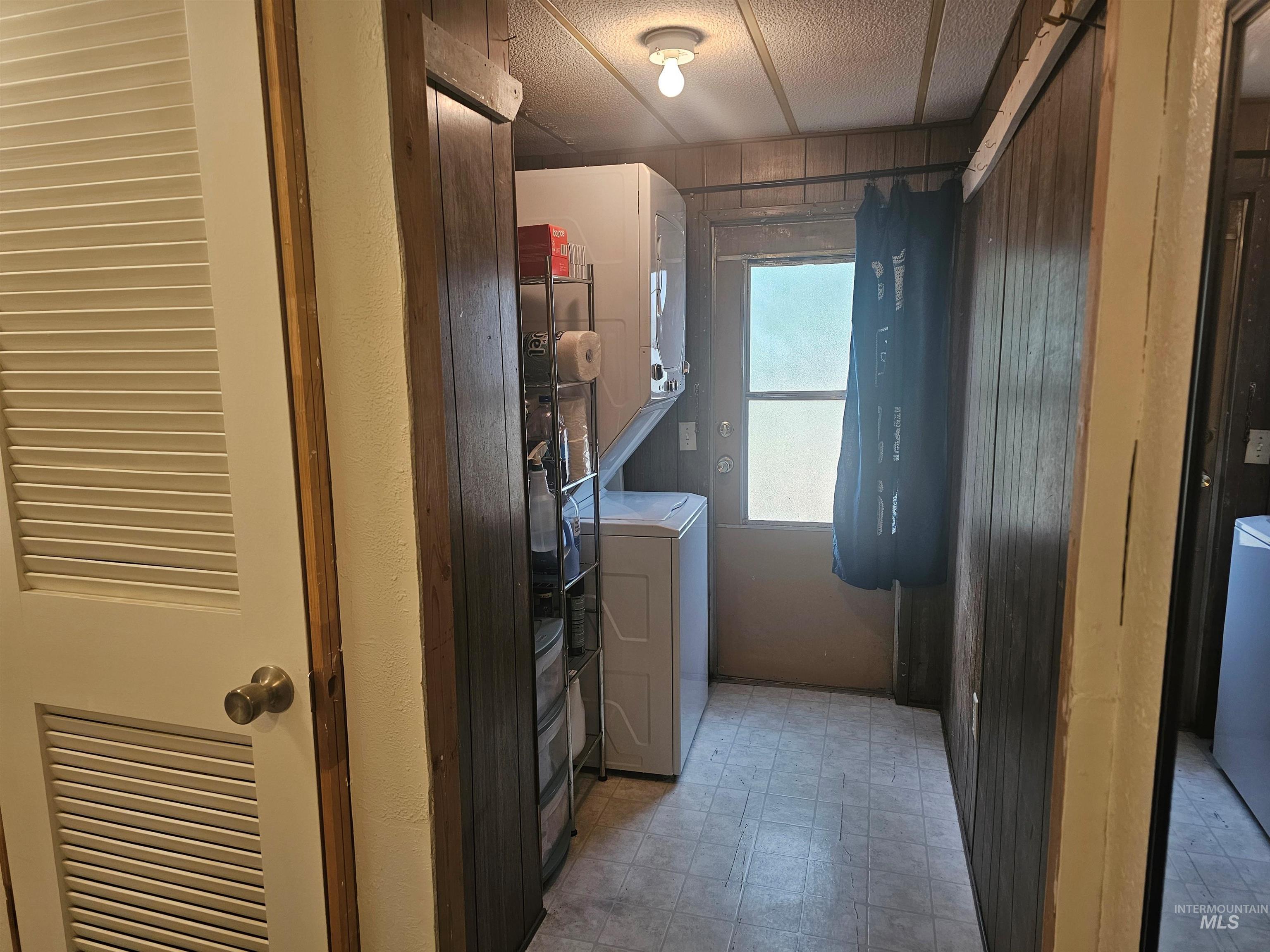 Washroom with light floors, stacked washing machine and dryer, and wooden walls