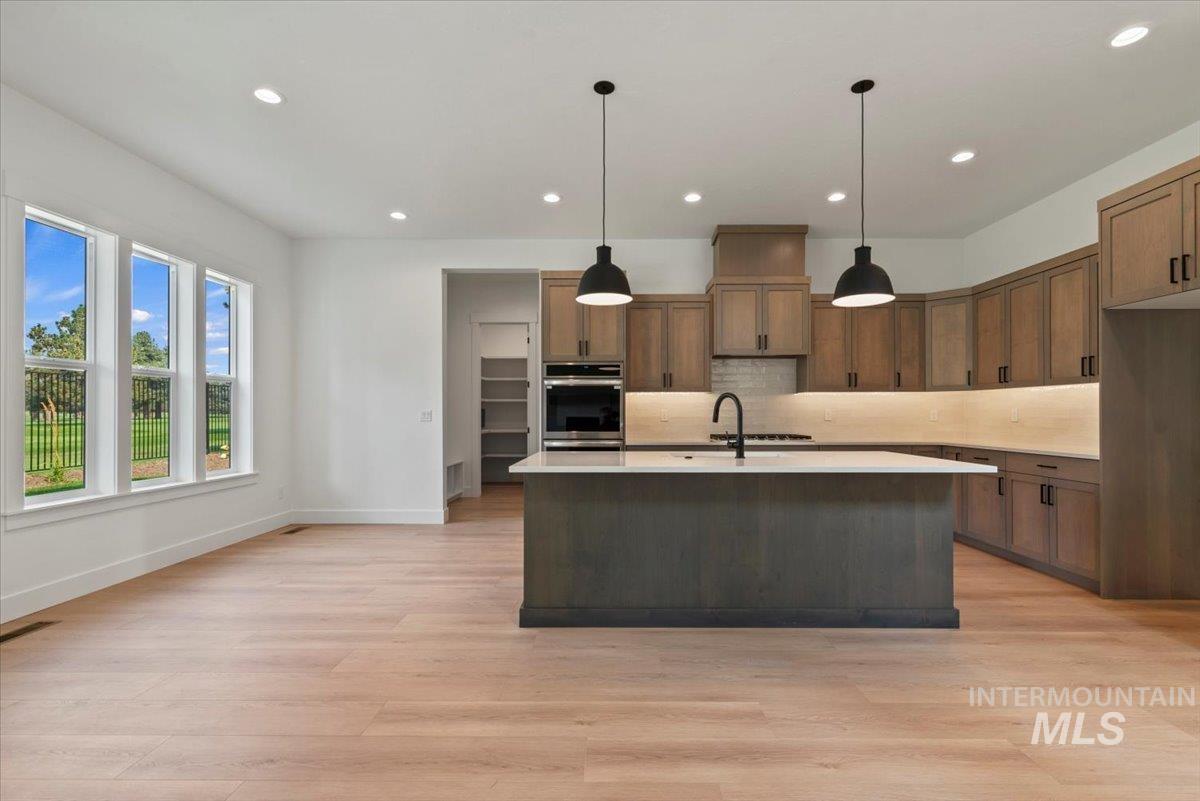 Kitchen with decorative light fixtures, backsplash, an island with sink, recessed lighting, and brown cabinets