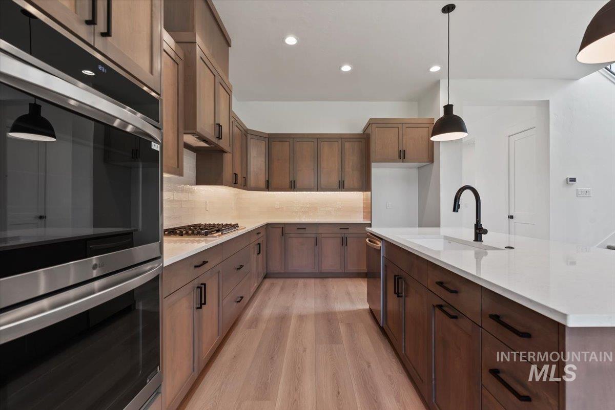 Kitchen featuring appliances with stainless steel finishes, decorative light fixtures, recessed lighting, light wood-type flooring, and decorative backsplash