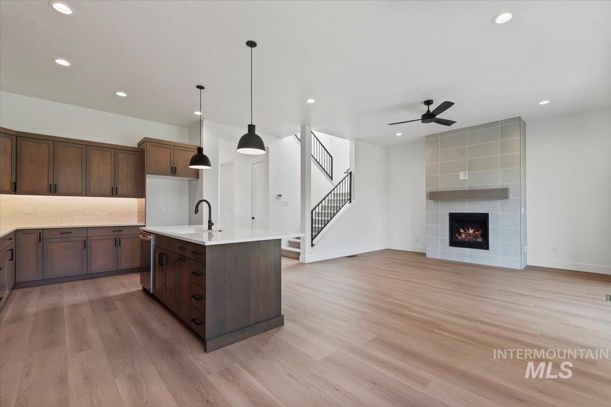 Kitchen featuring pendant lighting, light wood-type flooring, recessed lighting, a tiled fireplace, and a center island with sink