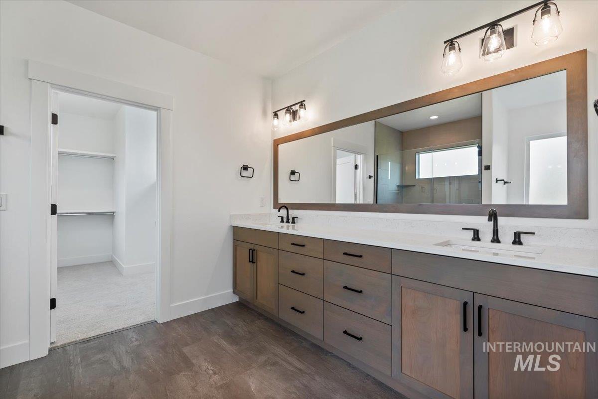 Full bath with walk in shower, dark wood-style flooring, double vanity, and a spacious closet