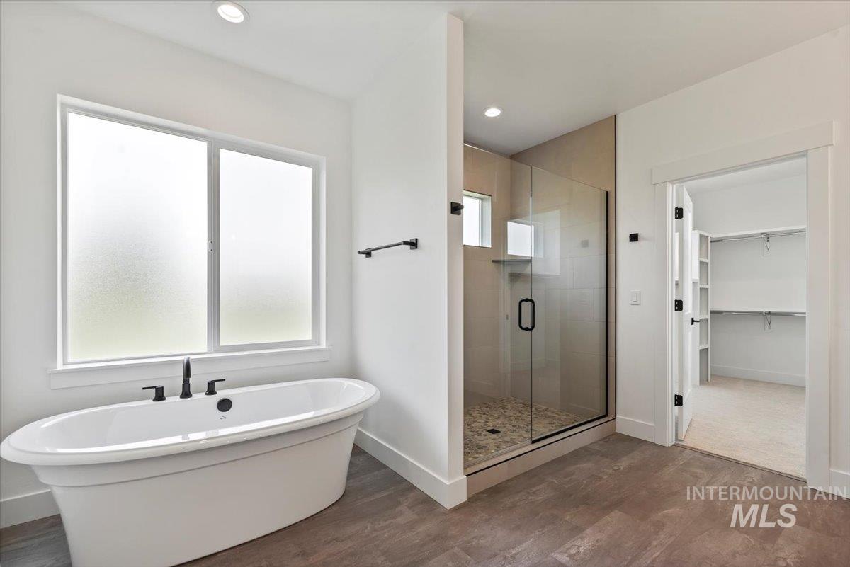 Full bath featuring a stall shower, a freestanding bath, dark wood-style floors, a spacious closet, and recessed lighting