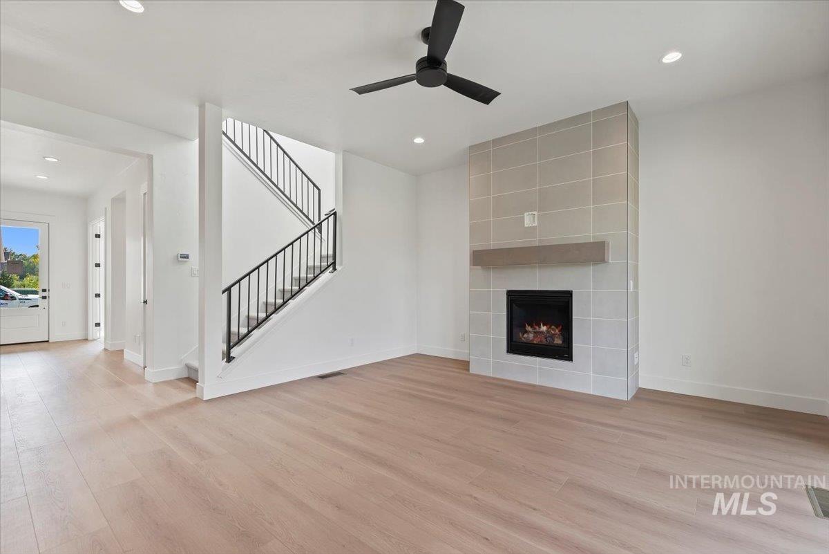 Unfurnished living room with light wood-style flooring, recessed lighting, a fireplace, stairs, and ceiling fan