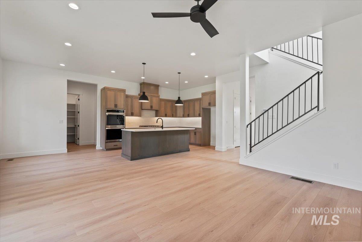 Kitchen with light countertops, open floor plan, pendant lighting, light wood finished floors, and a kitchen island with sink