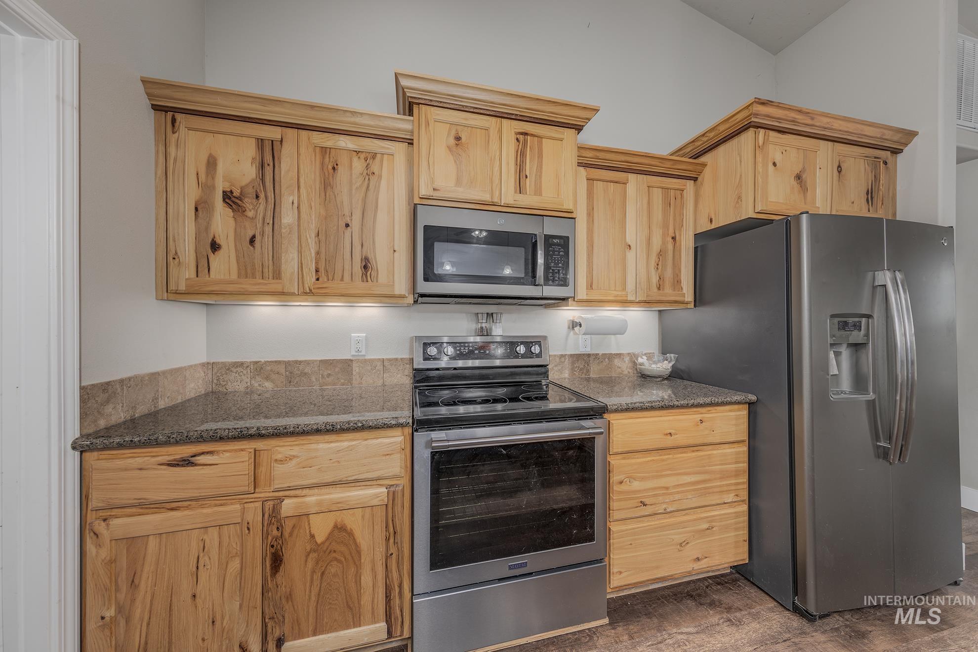 Kitchen with stainless steel appliances, dark stone counters, light brown cabinets, and dark wood-style flooring