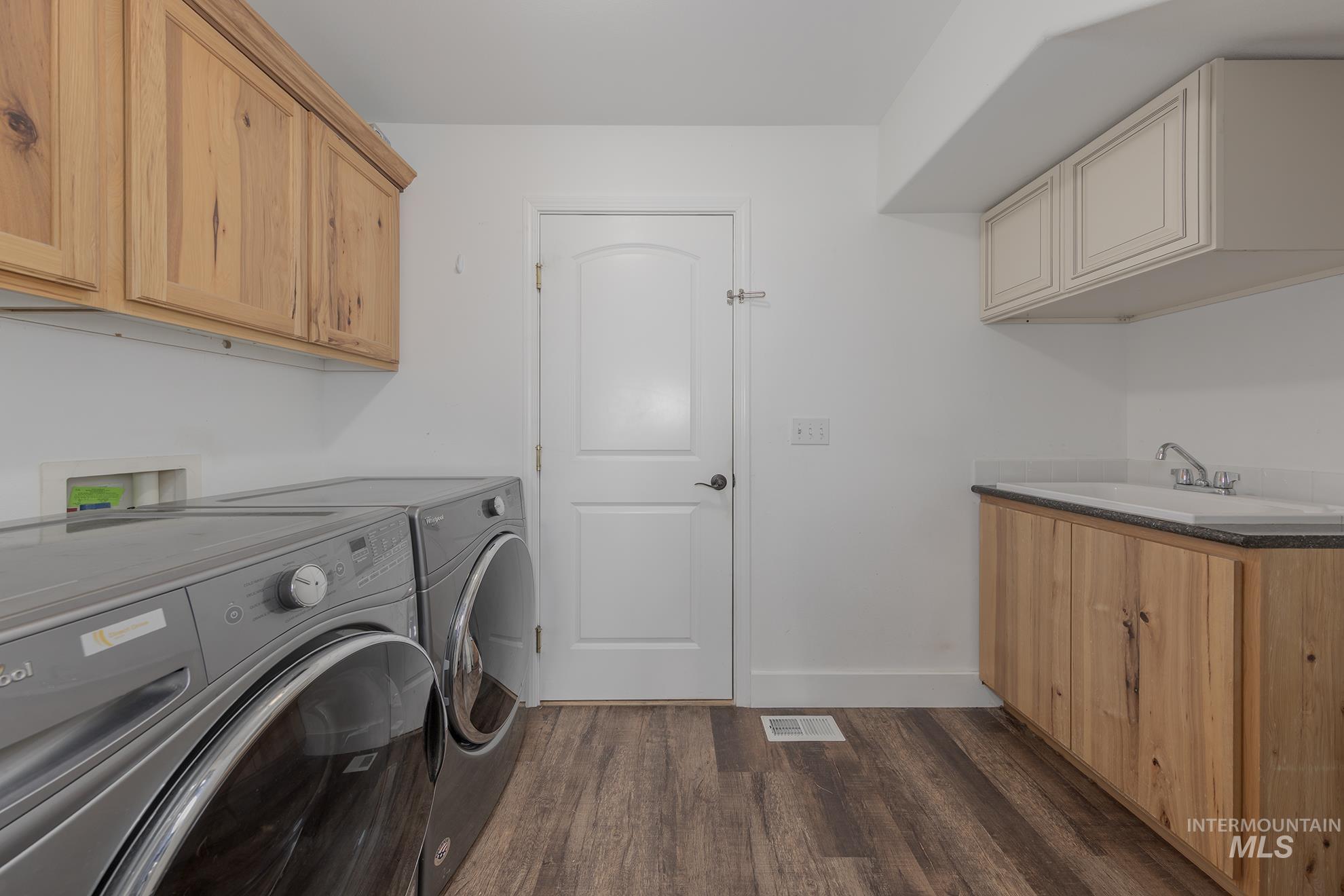 Laundry room with dark wood finished floors, cabinet space, and washing machine and clothes dryer