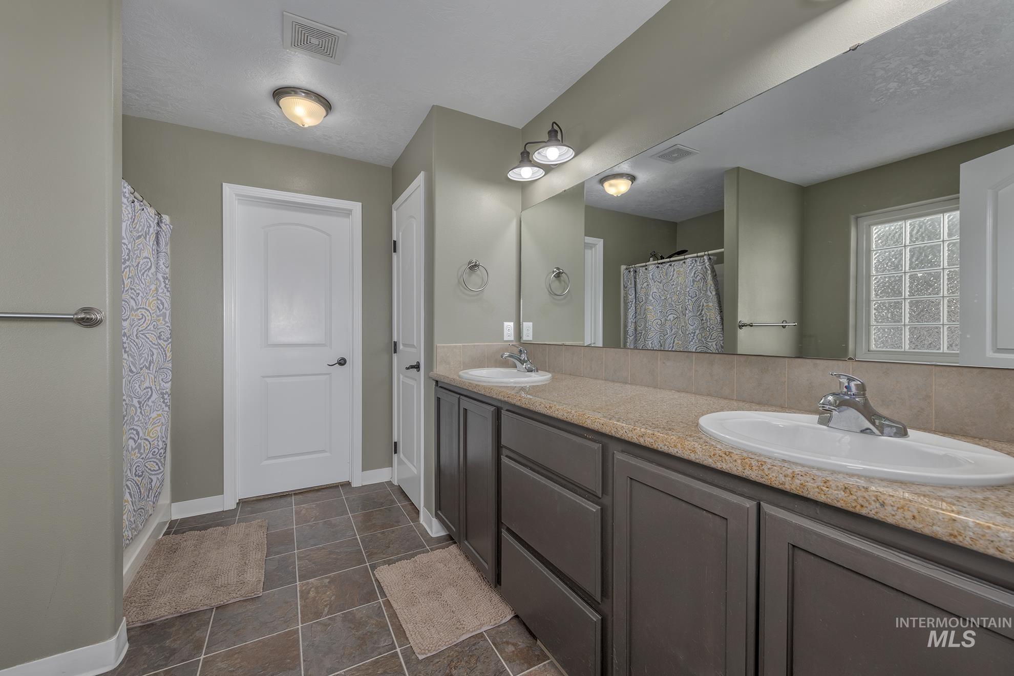 Full bath with double vanity, a textured ceiling, and a shower with curtain