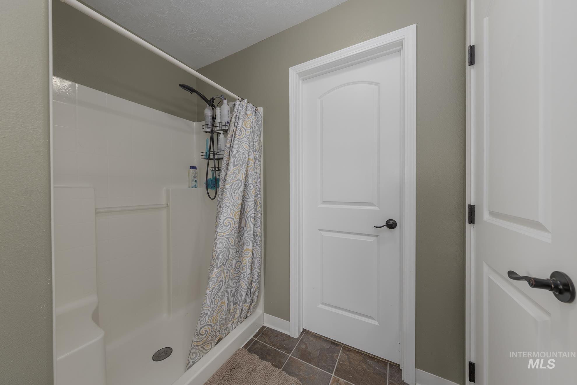 Bathroom featuring a shower stall and dark tile patterned flooring