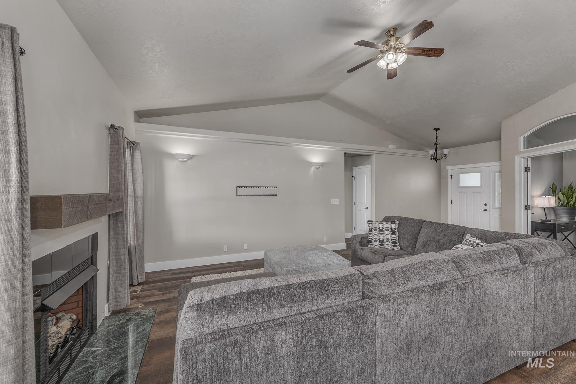 Living room featuring dark wood-style floors, vaulted ceiling, a tile fireplace, a ceiling fan, and a chandelier