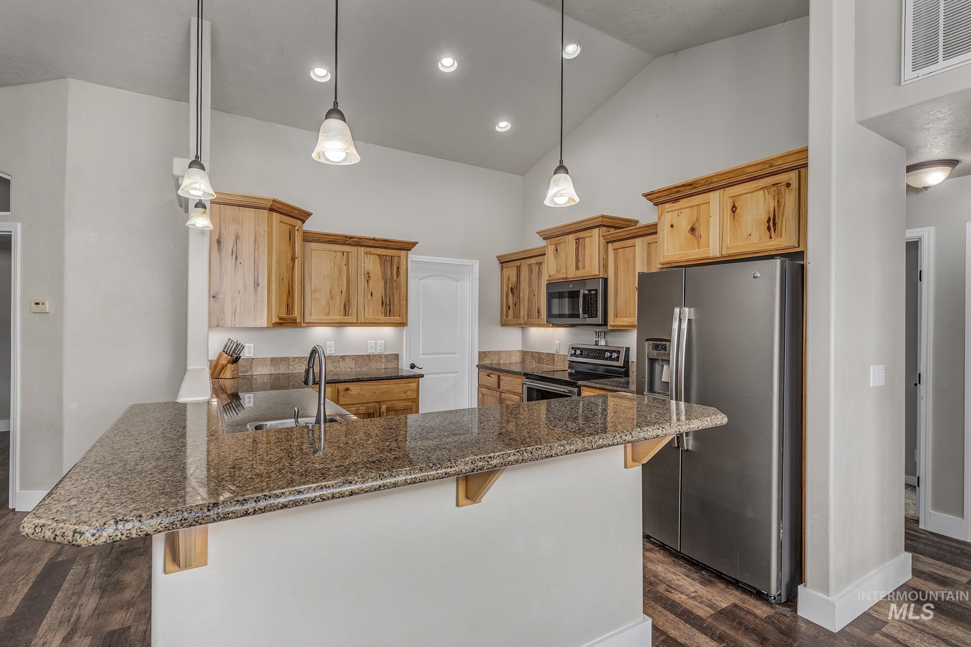 Kitchen with a breakfast bar, appliances with stainless steel finishes, pendant lighting, a peninsula, and high vaulted ceiling