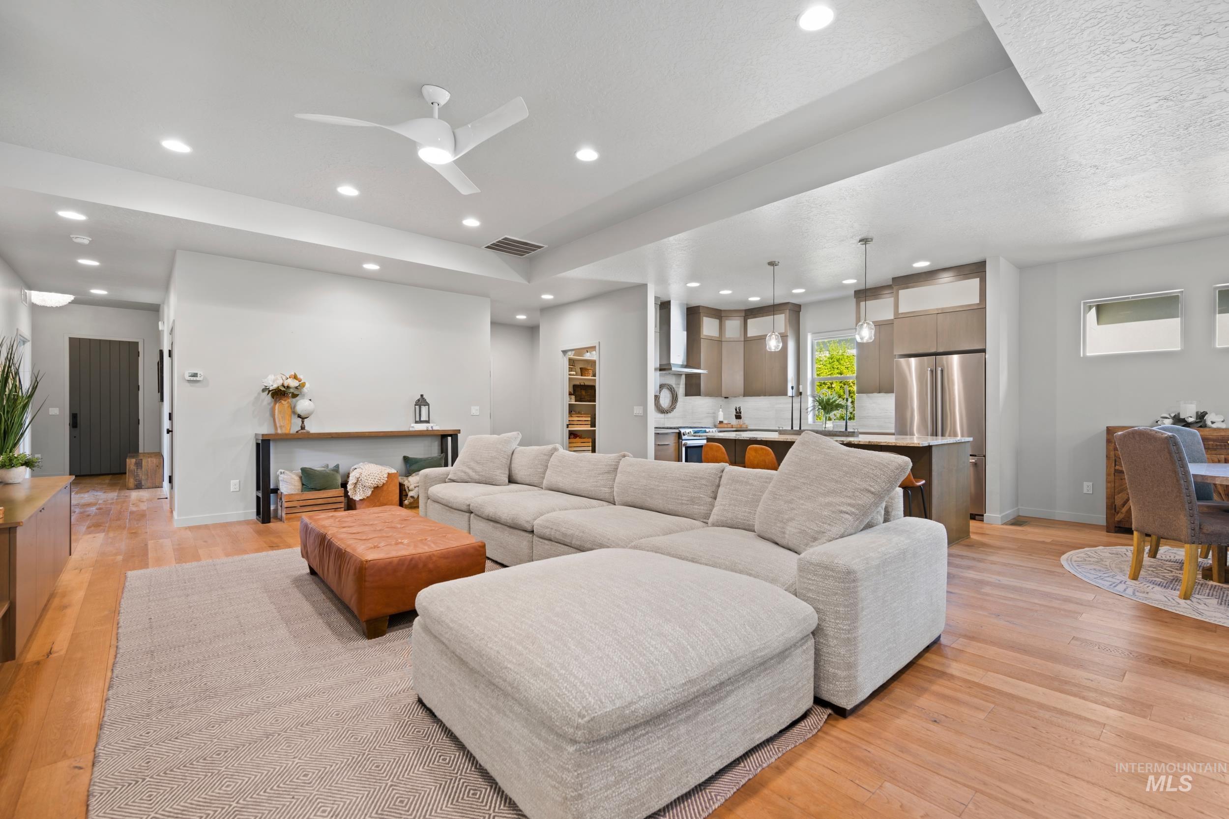 Living room featuring ceiling fan, a tray ceiling, recessed lighting, light wood finished floors, and a textured ceiling