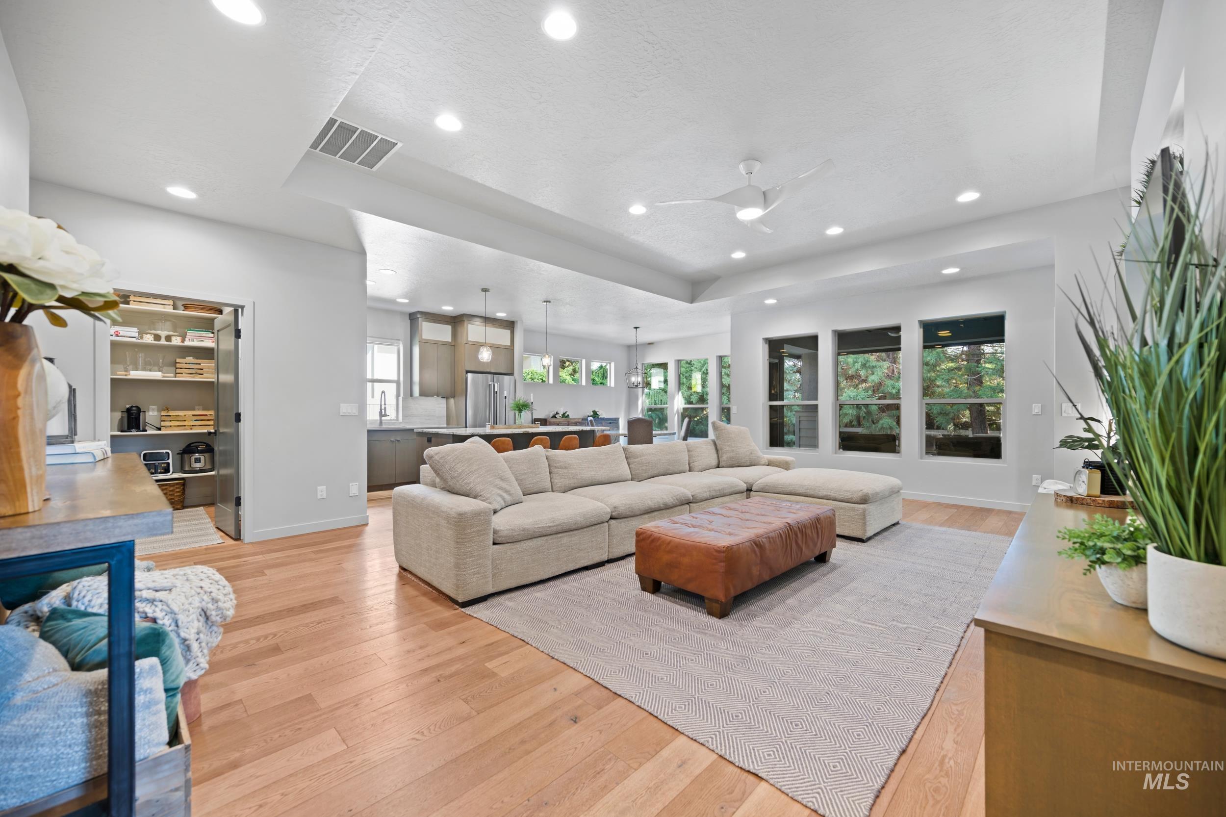 Living room with a tray ceiling, light wood finished floors, ceiling fan, and recessed lighting