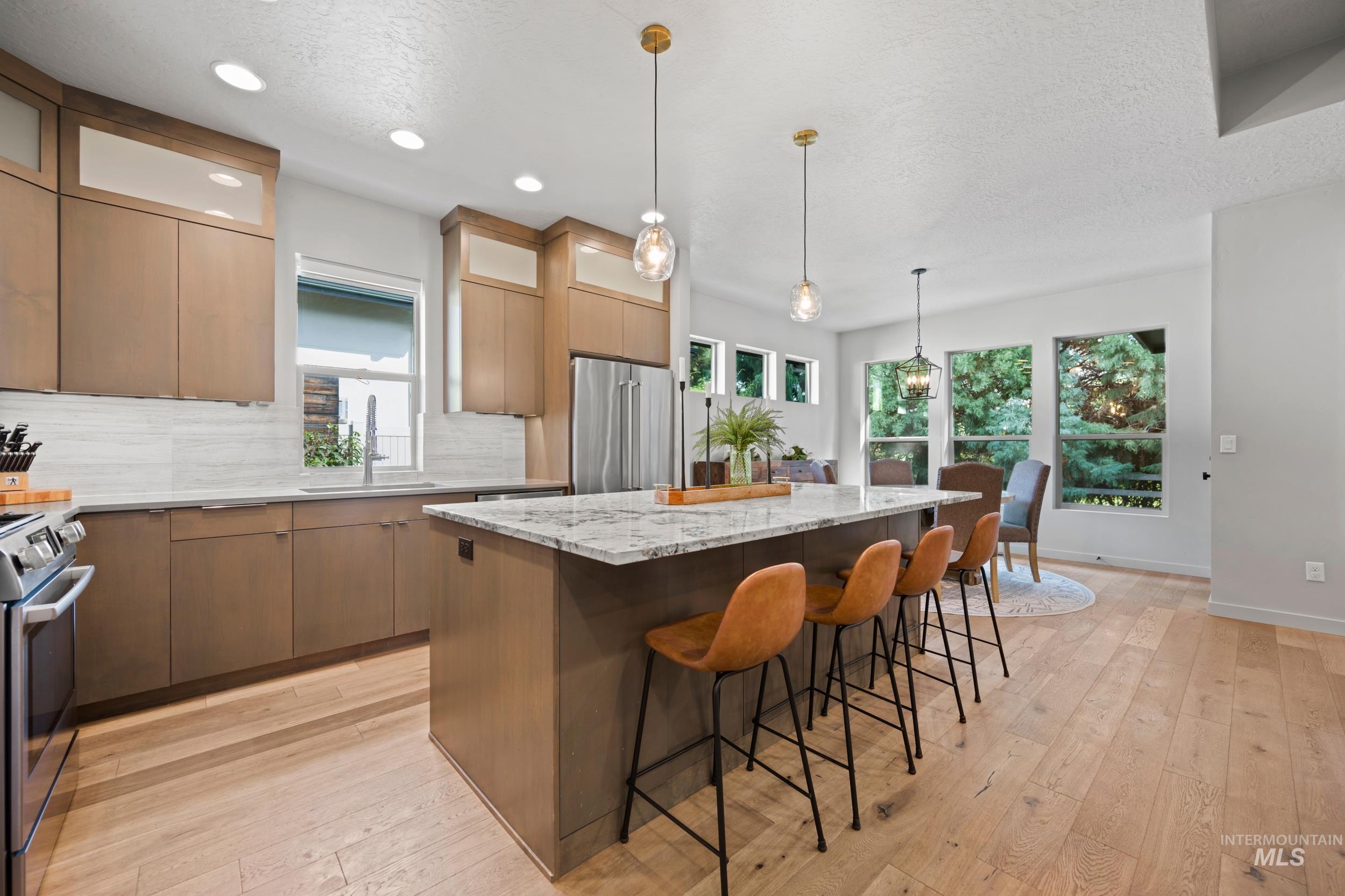 Kitchen featuring light stone countertops, light wood finished floors, a kitchen island, decorative light fixtures, and a textured ceiling