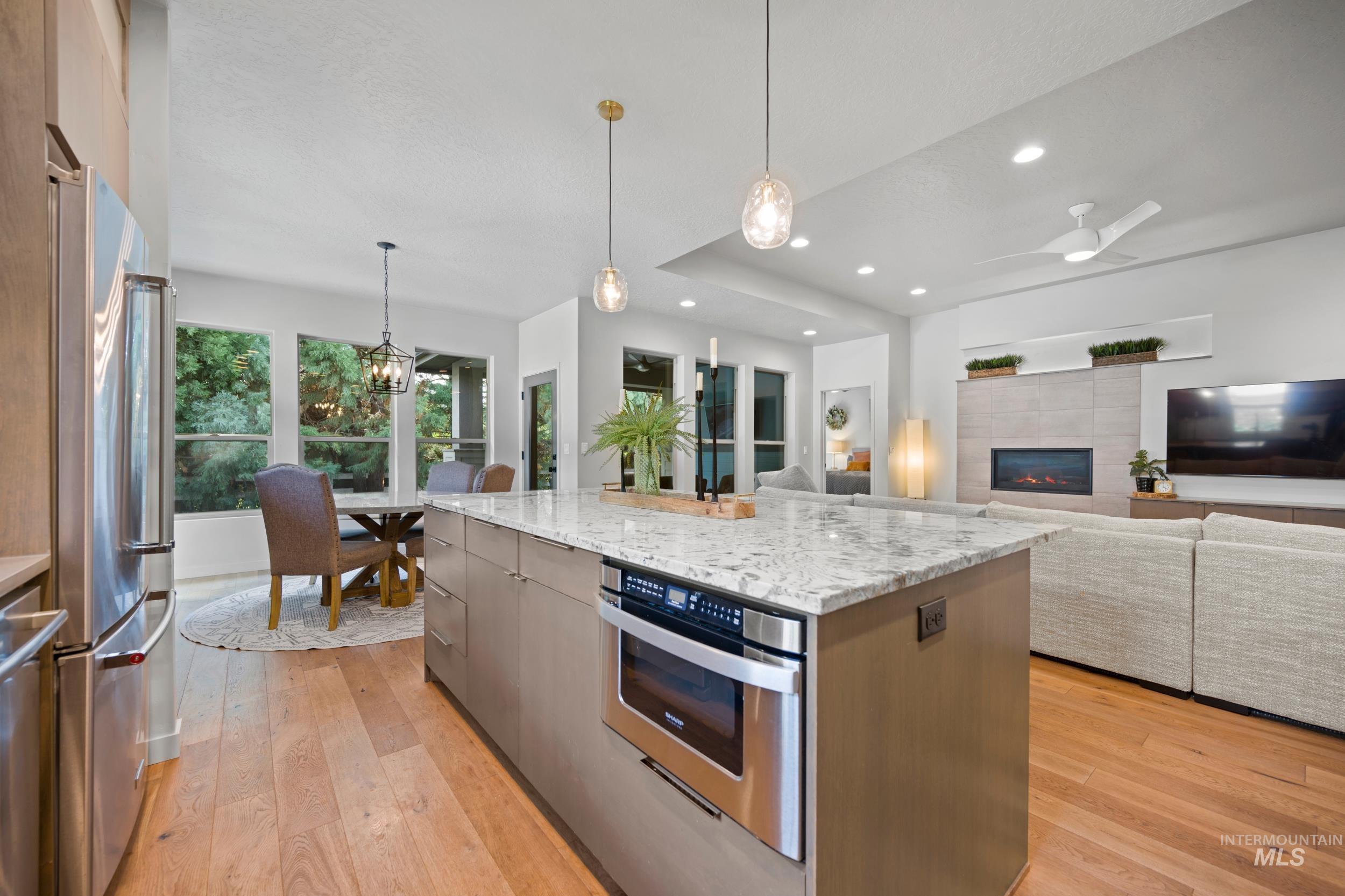 Kitchen with decorative light fixtures, light stone counters, modern cabinets, a tiled fireplace, and light wood-style flooring