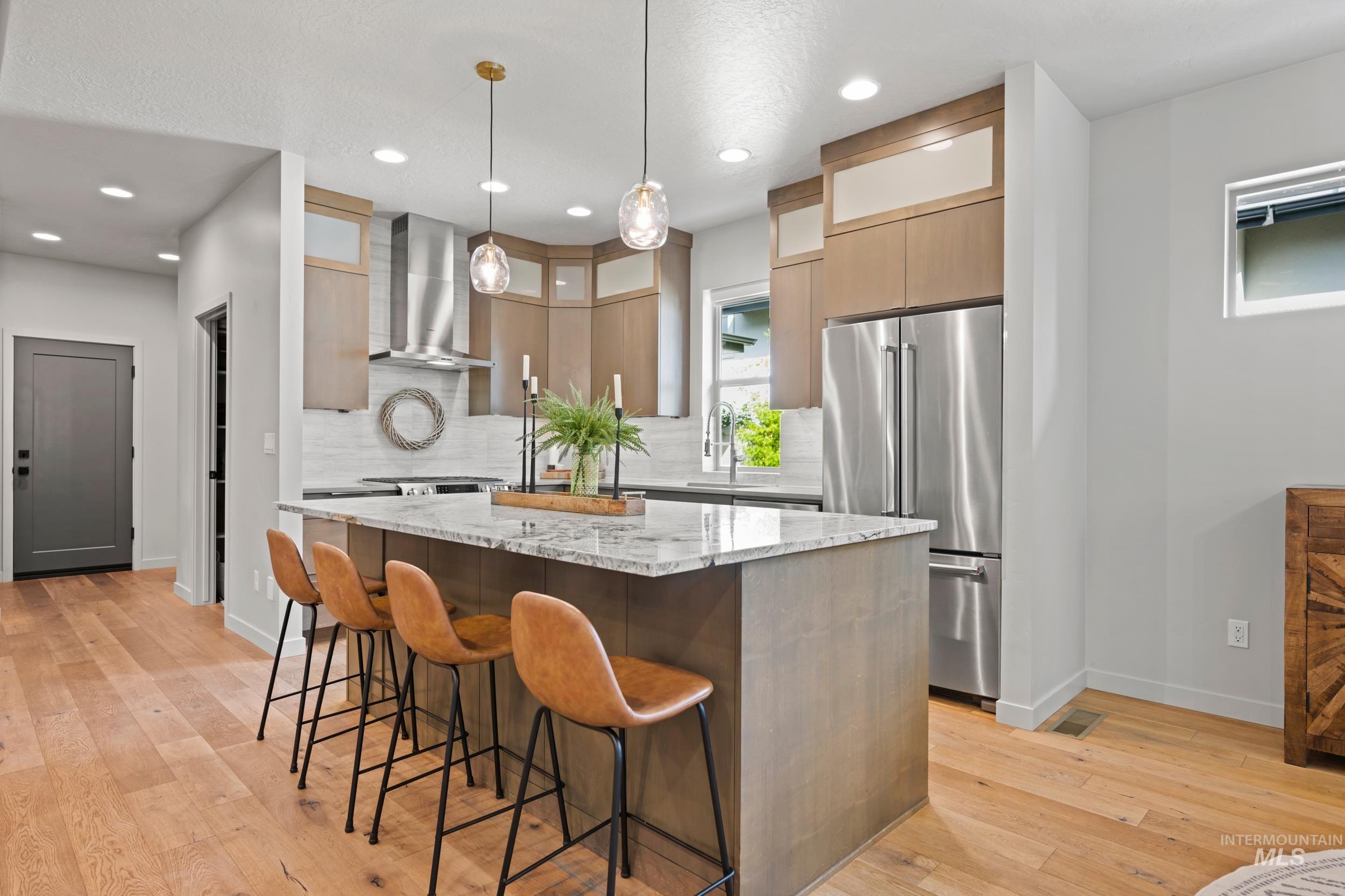 Kitchen featuring a breakfast bar, light stone countertops, freestanding refrigerator, pendant lighting, and a center island