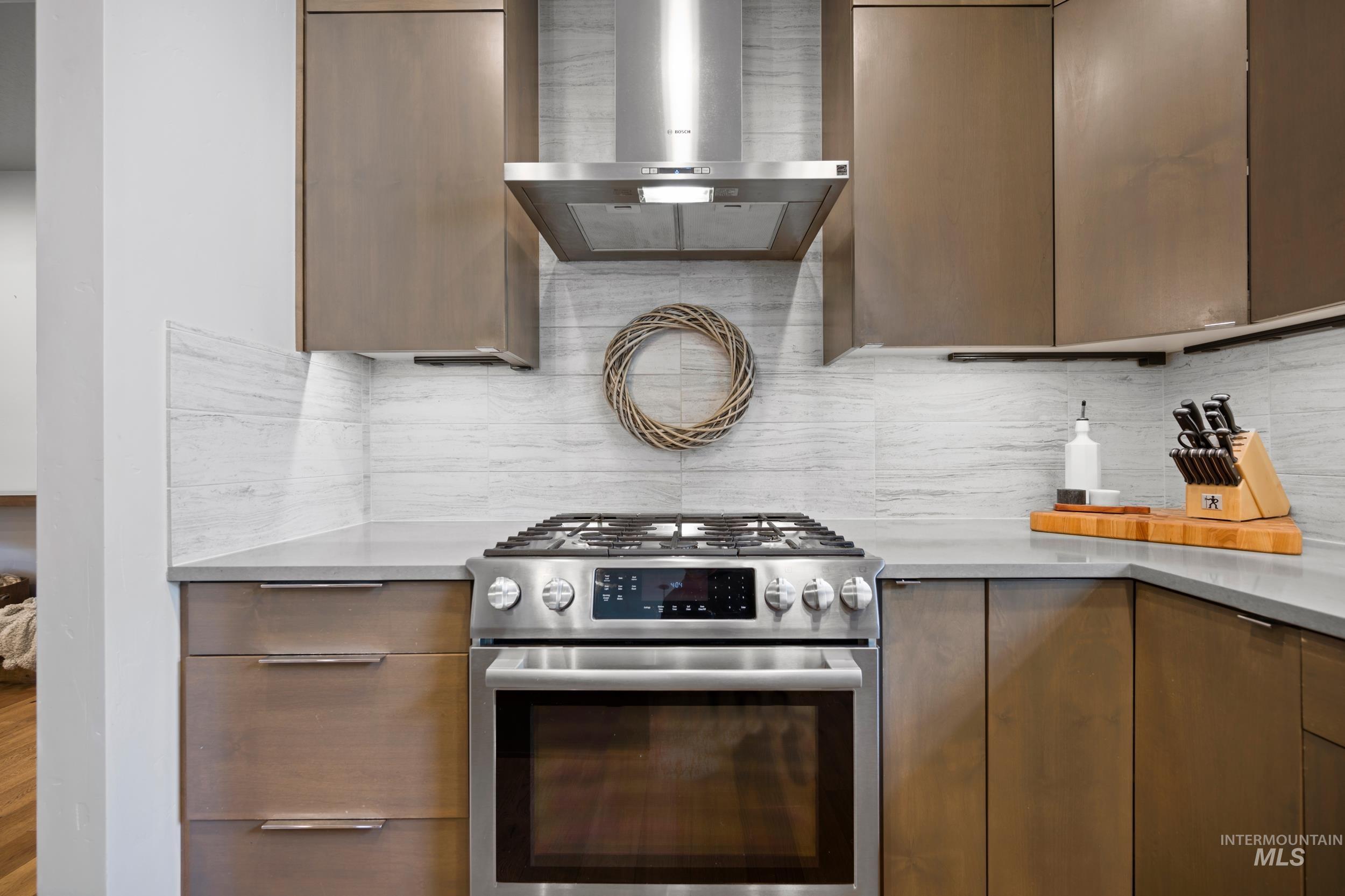 Kitchen featuring stainless steel range with gas stovetop, wall chimney exhaust hood, modern cabinets, decorative backsplash, and light stone countertops