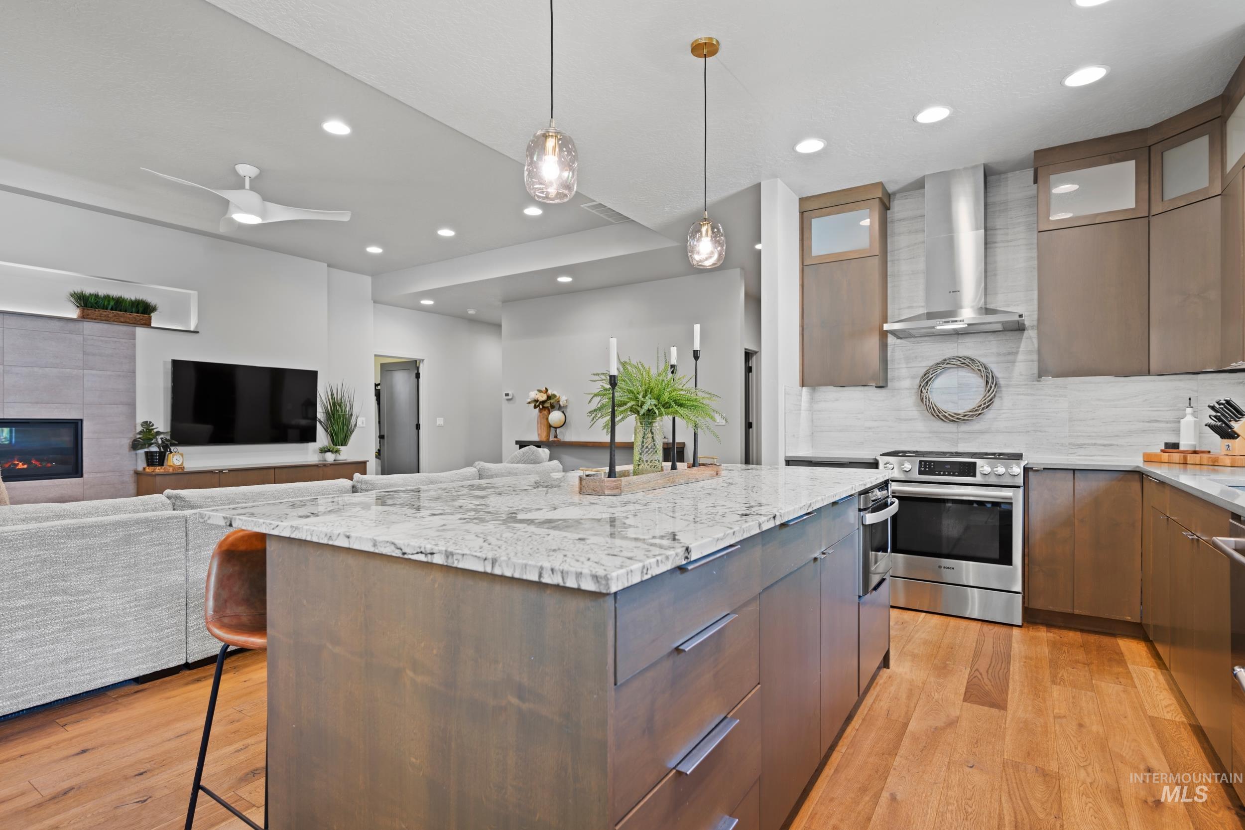 Kitchen with pendant lighting, a kitchen breakfast bar, light wood-style flooring, stainless steel appliances, and wall chimney range hood