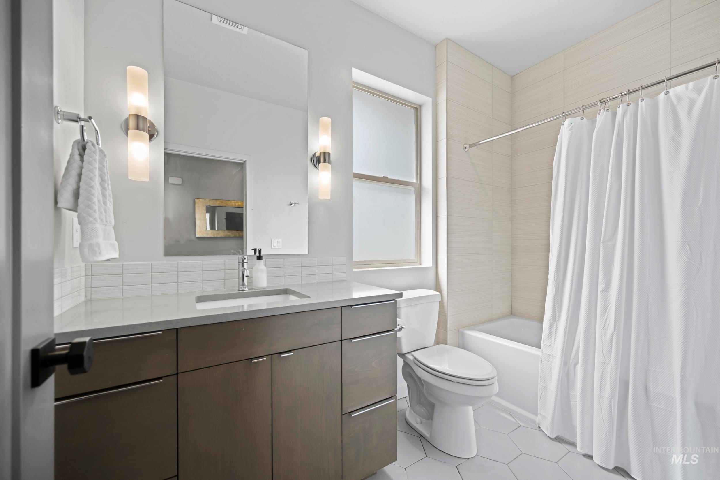 Full bathroom featuring vanity, shower / bath combo, light tile patterned floors, and decorative backsplash