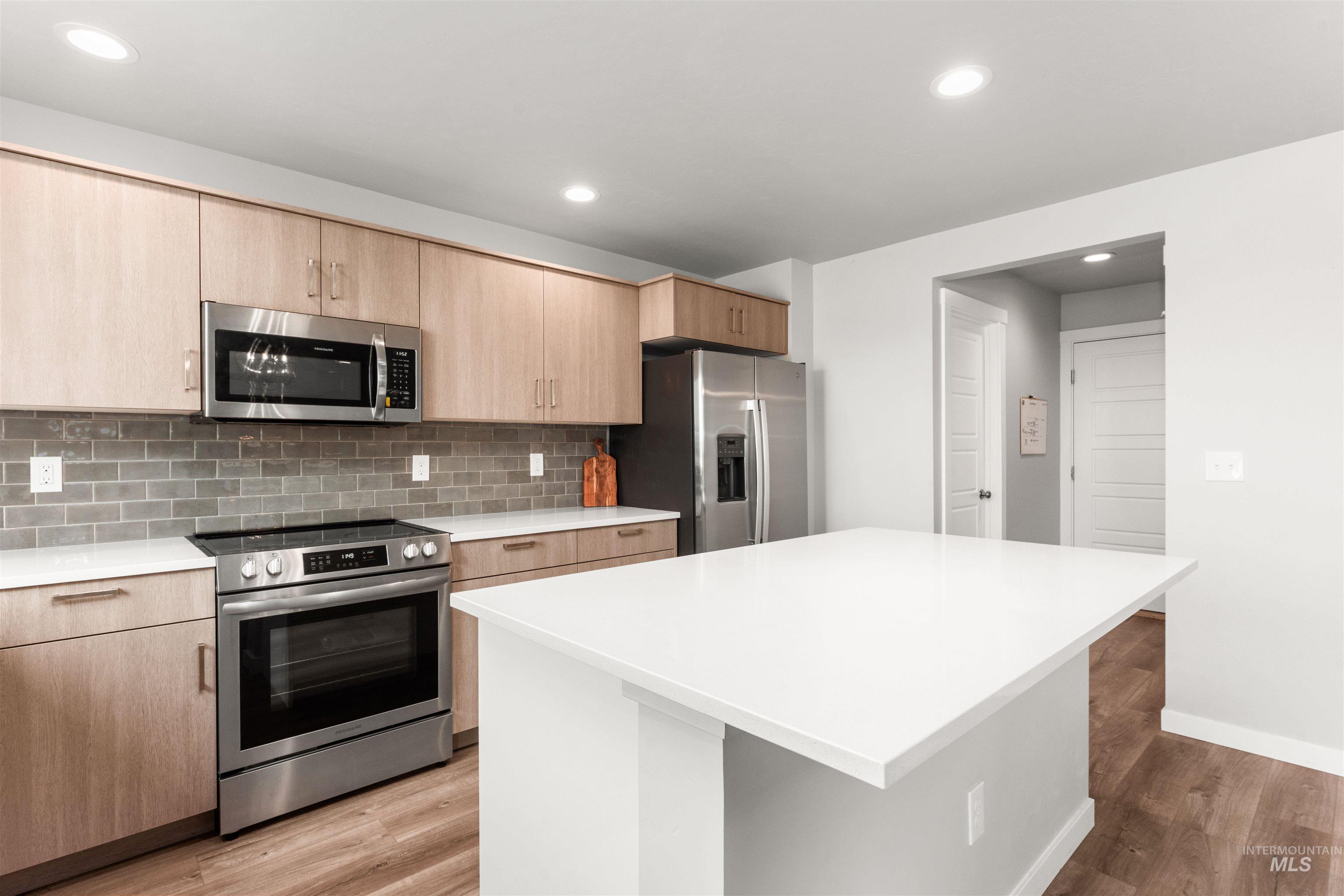 Kitchen with stainless steel appliances, backsplash, recessed lighting, light wood-style floors, and light brown cabinetry