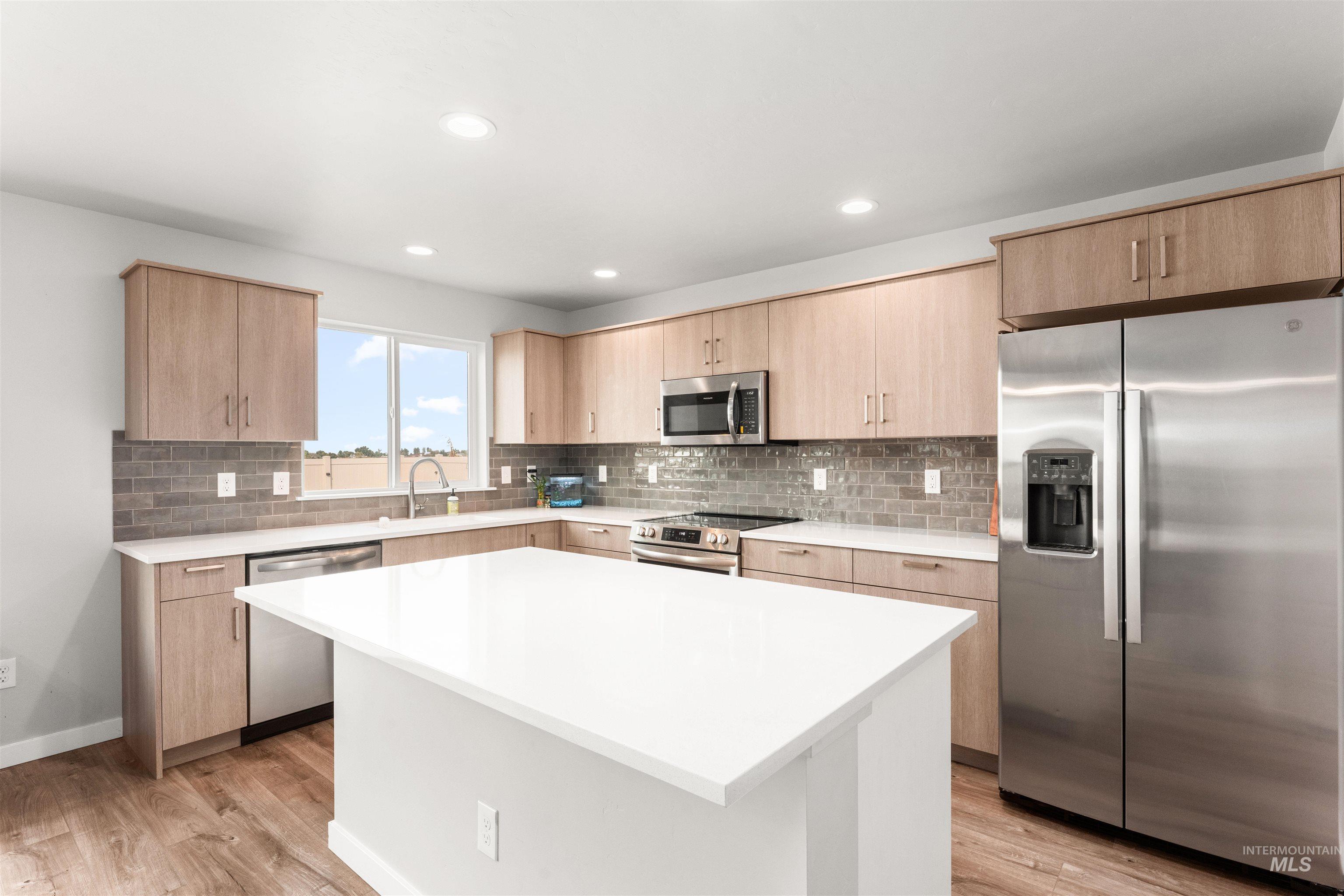 Kitchen with light brown cabinetry, appliances with stainless steel finishes, decorative backsplash, a center island, and recessed lighting