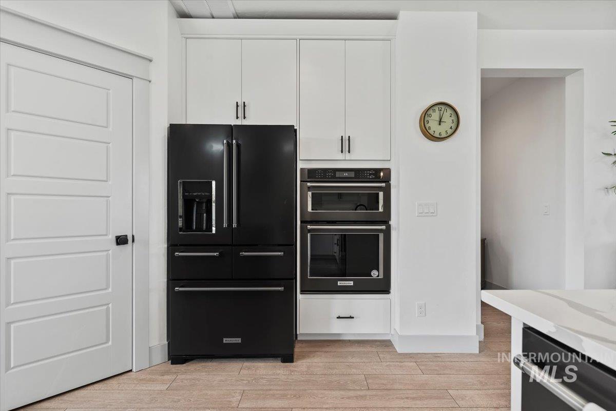 Kitchen with black appliances, light wood-style flooring, white cabinetry, and light countertops