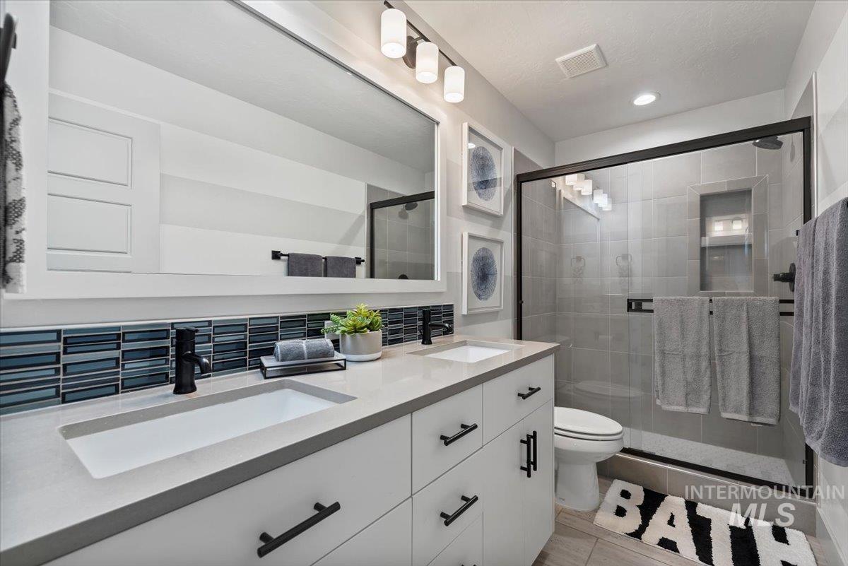 Full bath featuring double vanity, a stall shower, and tasteful backsplash