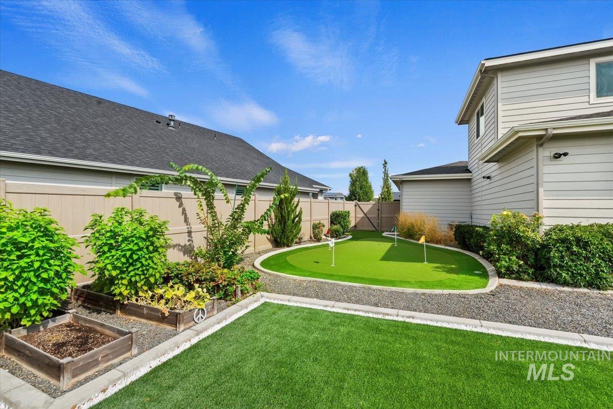 Fenced backyard featuring an area to practice putting and a vegetable garden