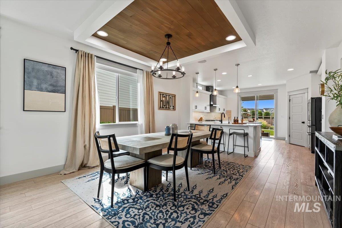 Dining area featuring a tray ceiling, wood ceiling, light wood-style flooring, recessed lighting, and a chandelier