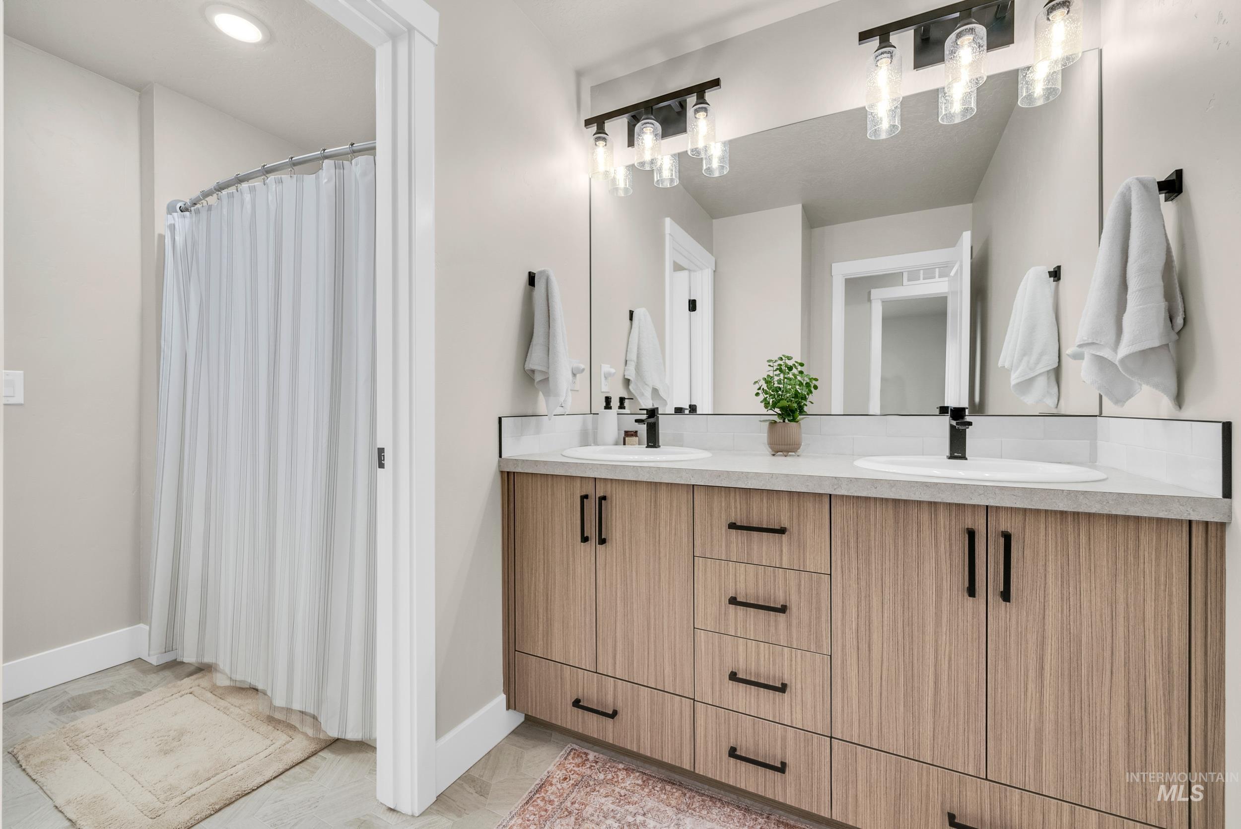 Bathroom with double vanity, curtained shower, and light tile patterned floors