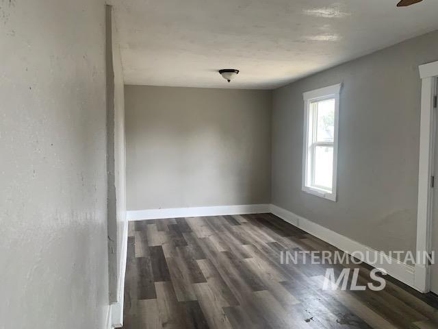 Spare room with dark wood-type flooring and baseboards
