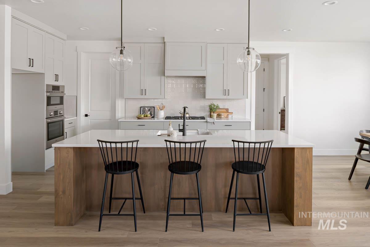Kitchen with a large island with sink, light wood finished floors, a kitchen breakfast bar, pendant lighting, and recessed lighting