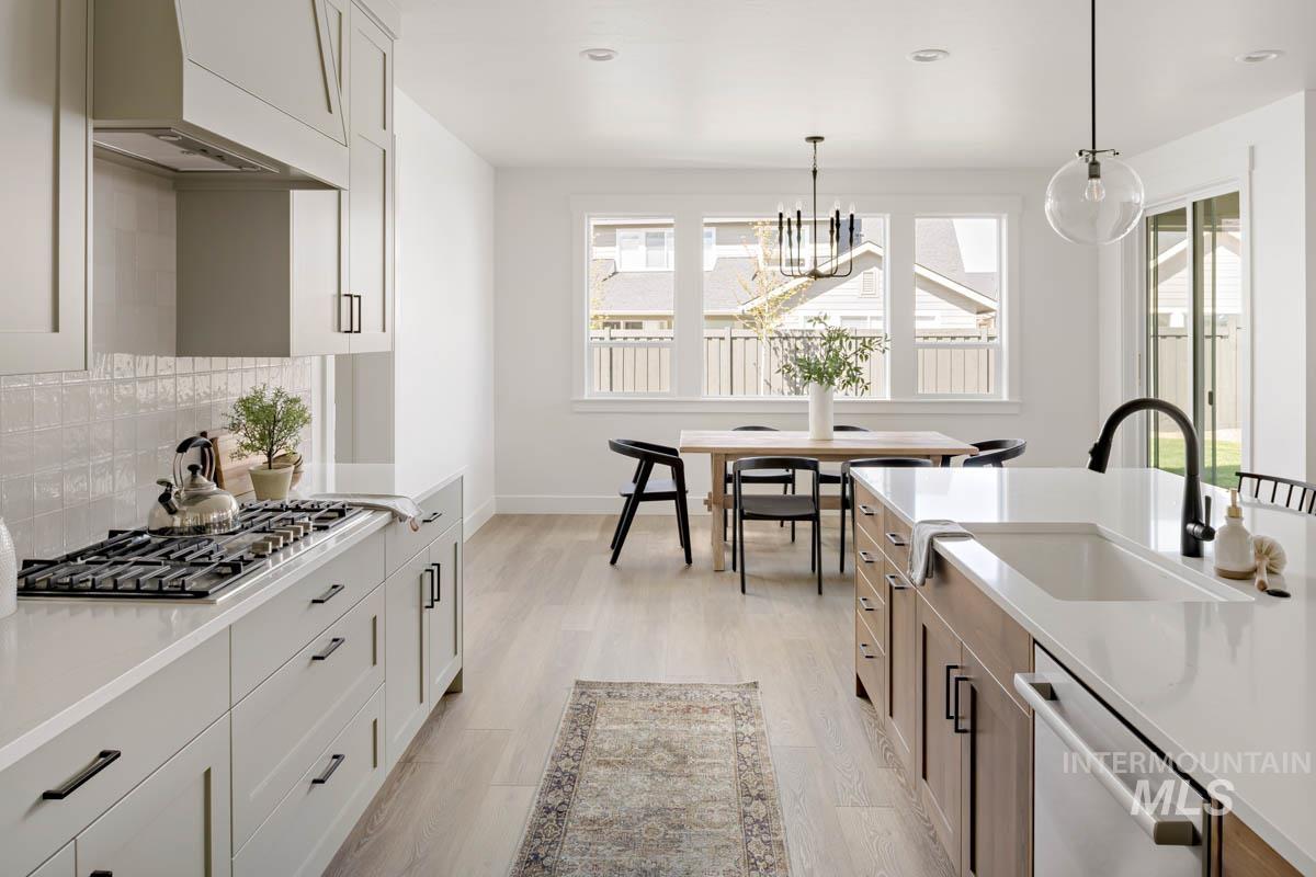 Kitchen featuring custom range hood, hanging light fixtures, light wood-style flooring, appliances with stainless steel finishes, and decorative backsplash