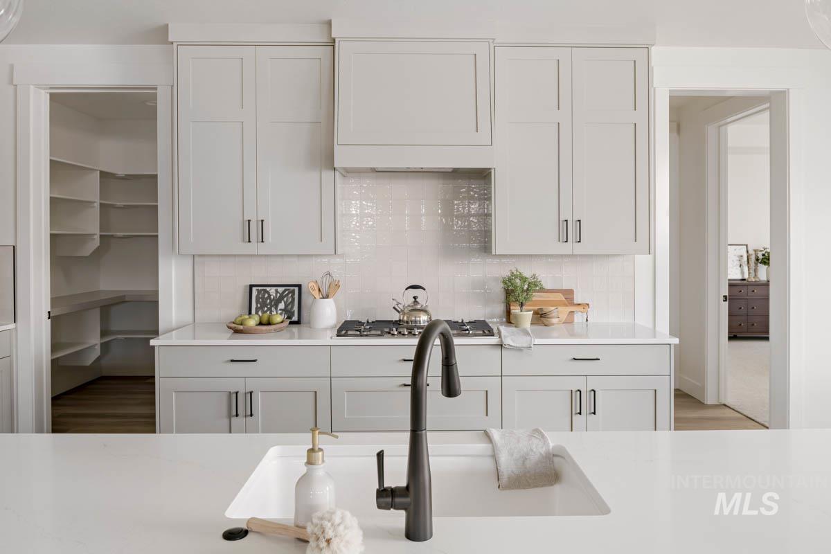 Kitchen with tasteful backsplash, light stone counters, white cabinetry, and stainless steel gas stovetop