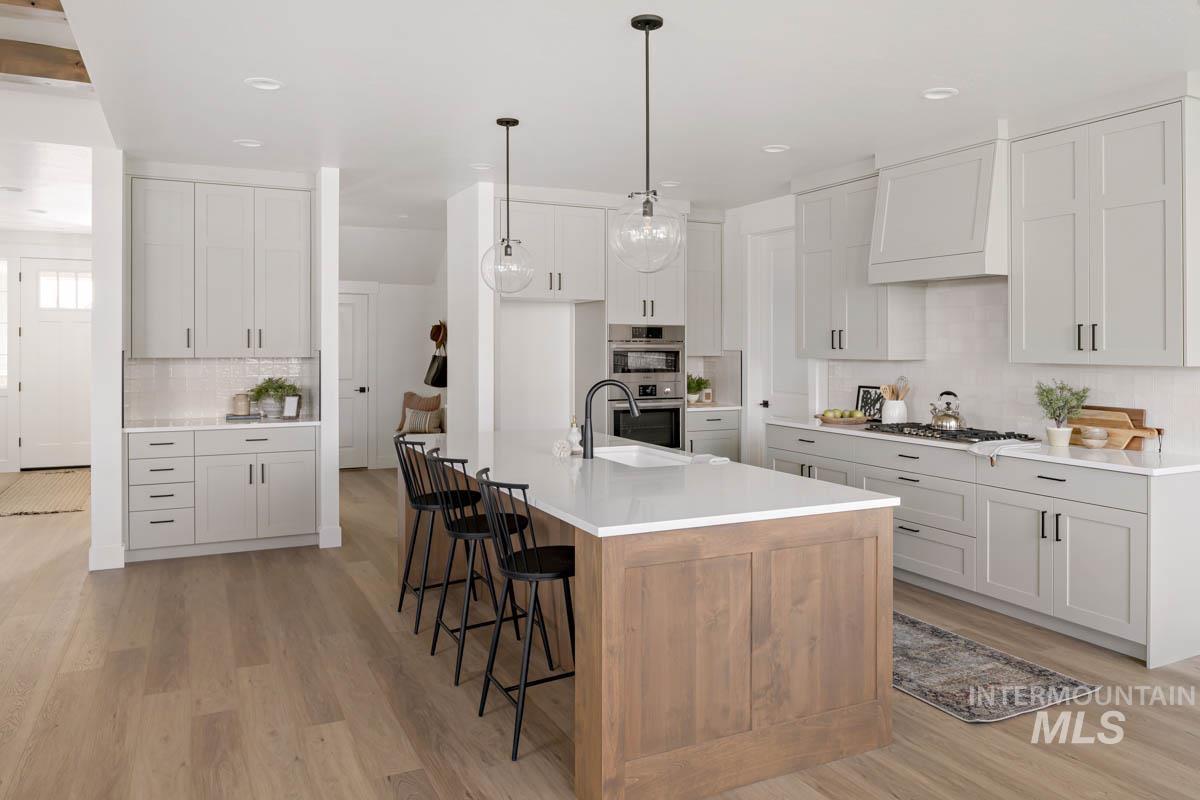 Kitchen featuring backsplash, a kitchen island with sink, light wood-style flooring, custom exhaust hood, and recessed lighting