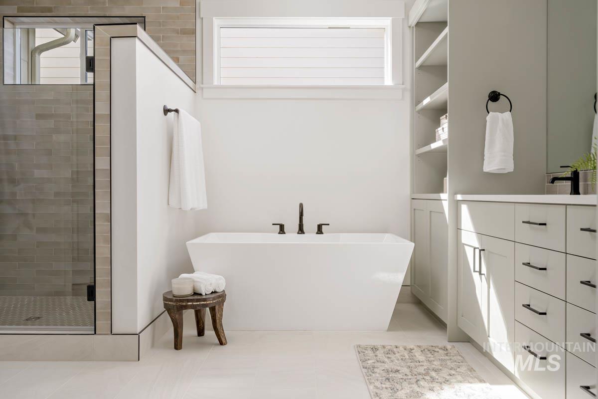 Bathroom featuring vanity, a freestanding tub, a stall shower, and light tile patterned floors