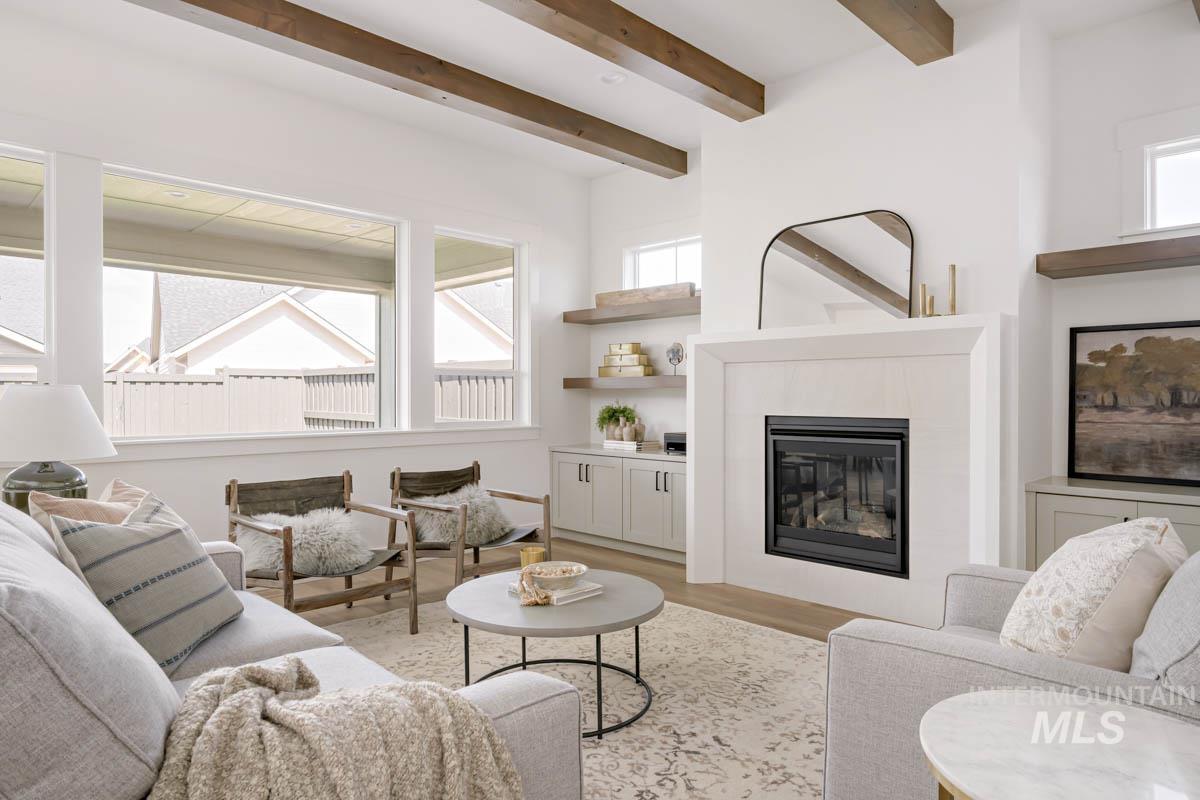 Living room with a tiled fireplace, light wood-type flooring, and beam ceiling