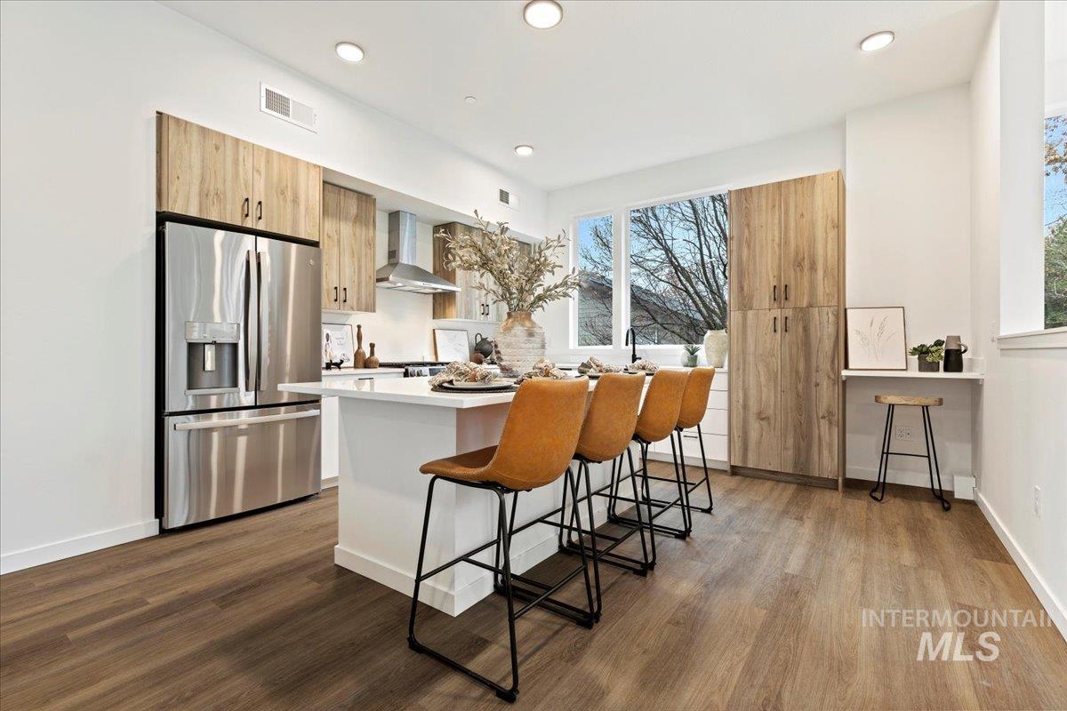 Kitchen with stainless steel fridge with ice dispenser, a kitchen bar, a center island, light brown cabinets, and modern cabinets