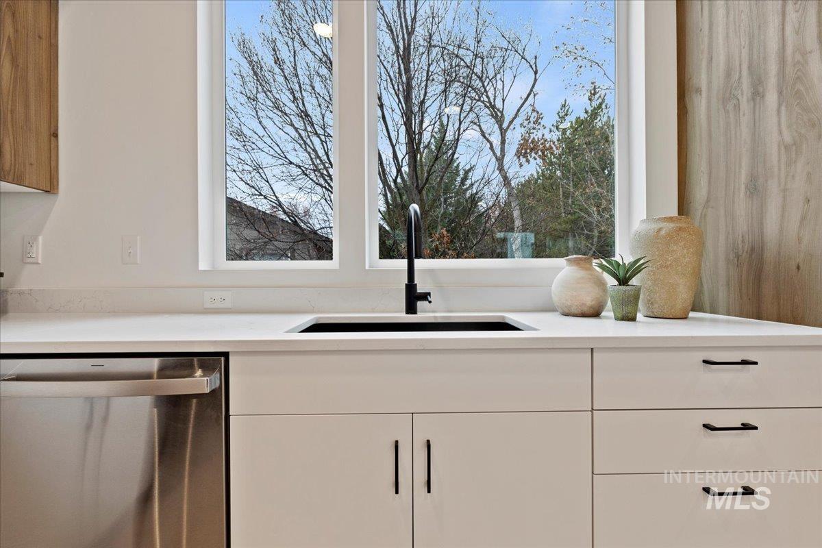 Kitchen view of stainless steel dishwasher, white cabinetry, and light stone countertops