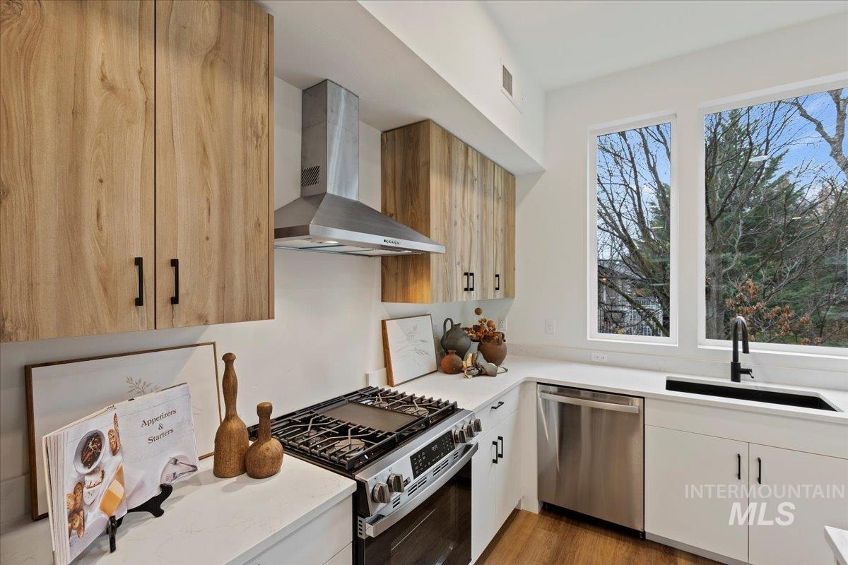Kitchen featuring appliances with stainless steel finishes, light stone counters, wall chimney exhaust hood, and light wood-type flooring
